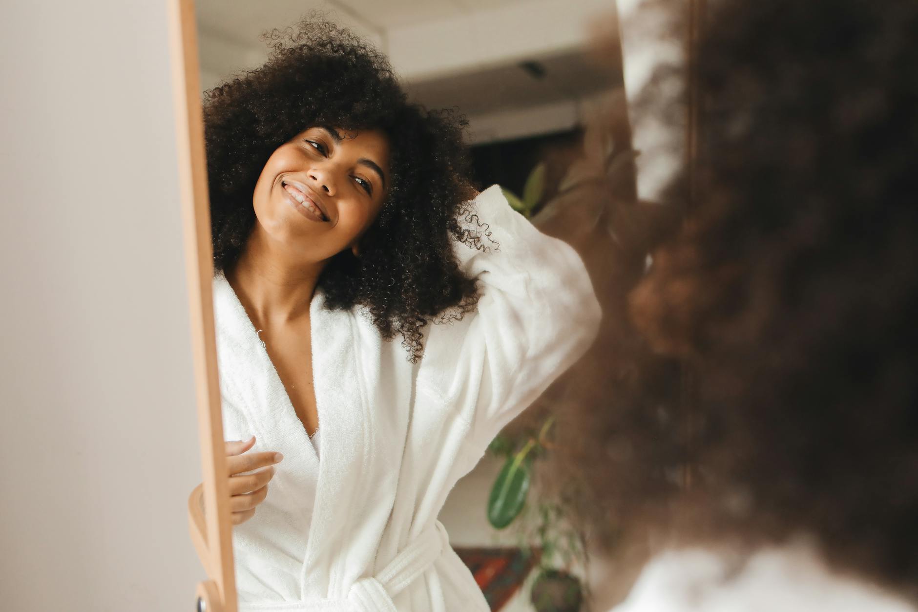 Happy woman with curly hair smiling in a bathrobe at home. - self care habits