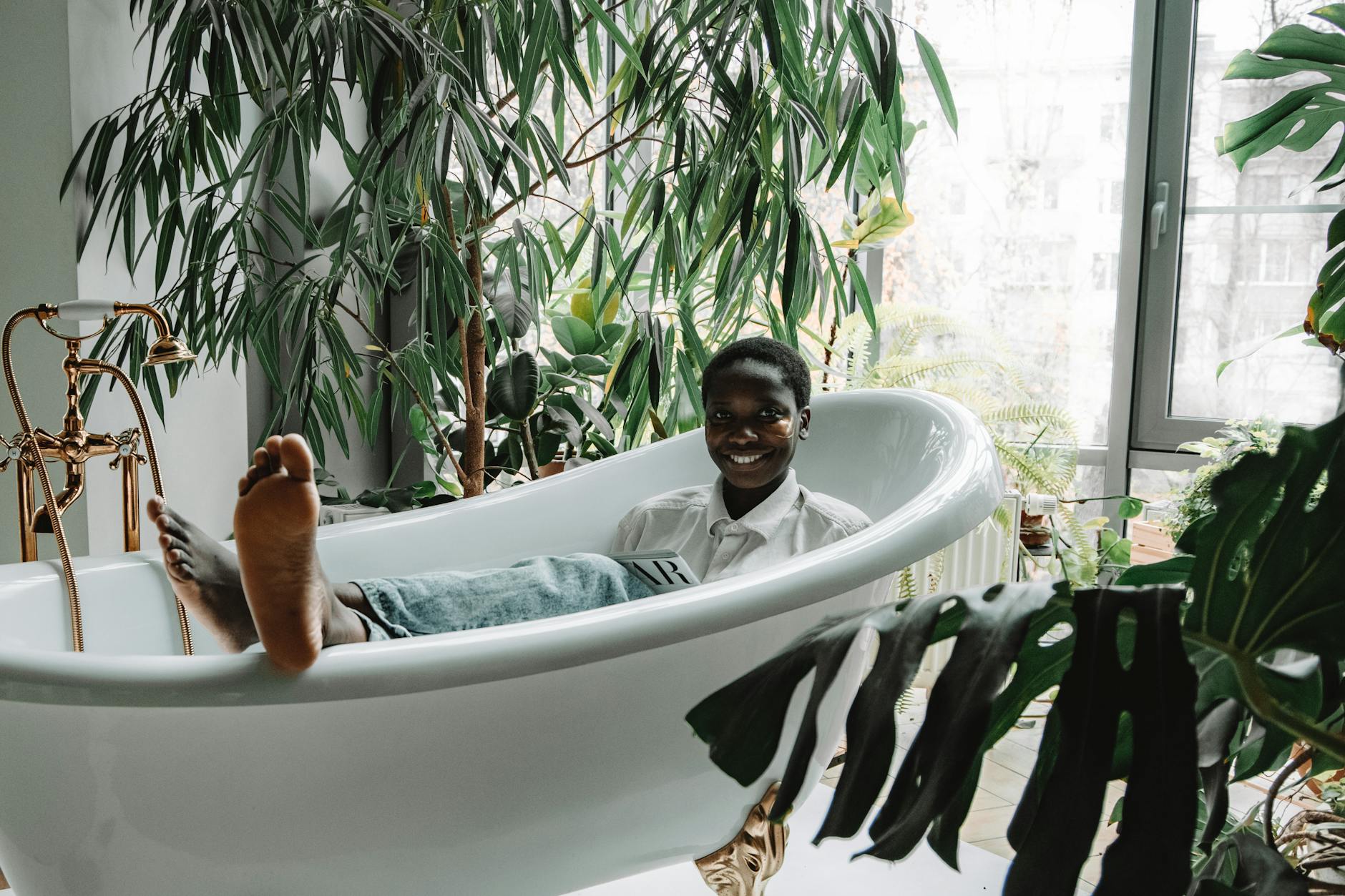 African American woman smiling in bathtub, surrounded by lush plants, enjoying a moment of self-care. - self care habits