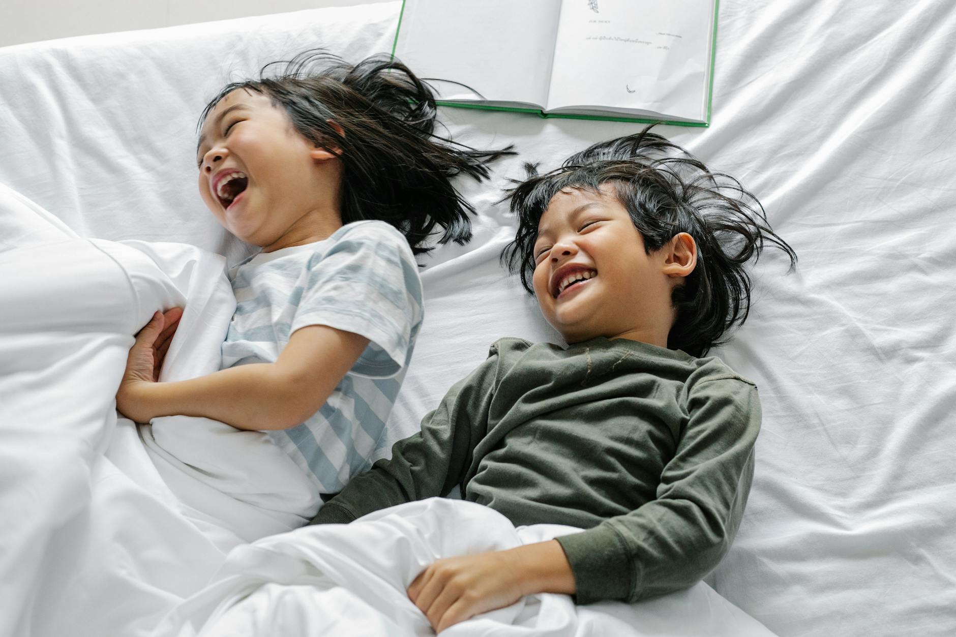 From above of Asian boy and girl laughing and smiling while lying in sleepwear on bed in morning n bedroom - sibling rivalry quotes