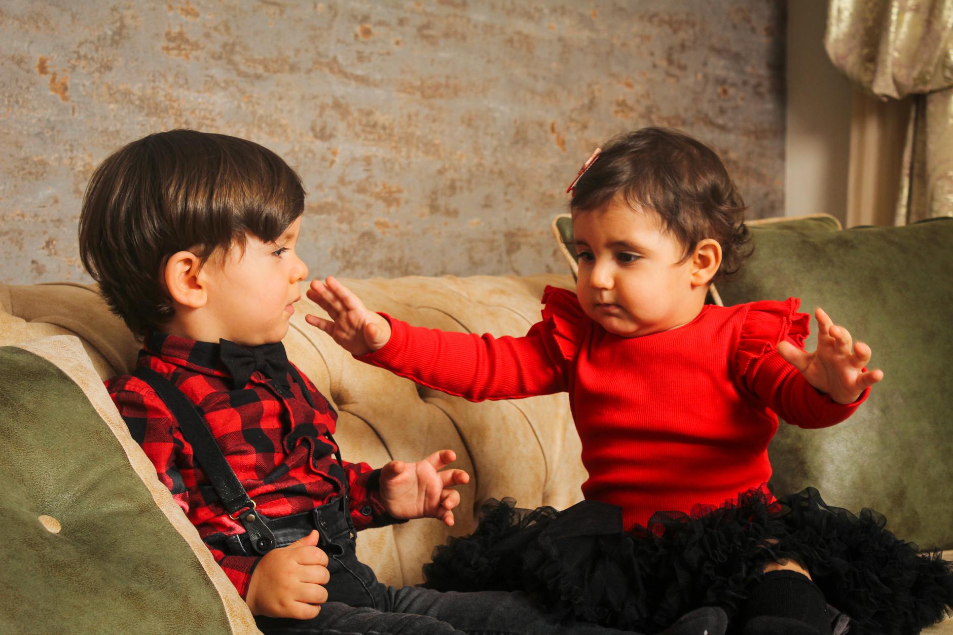 Charming siblings in stylish outfits sitting together on a sofa indoors, showcasing adorable family moments. - sibling rivalry quotes
