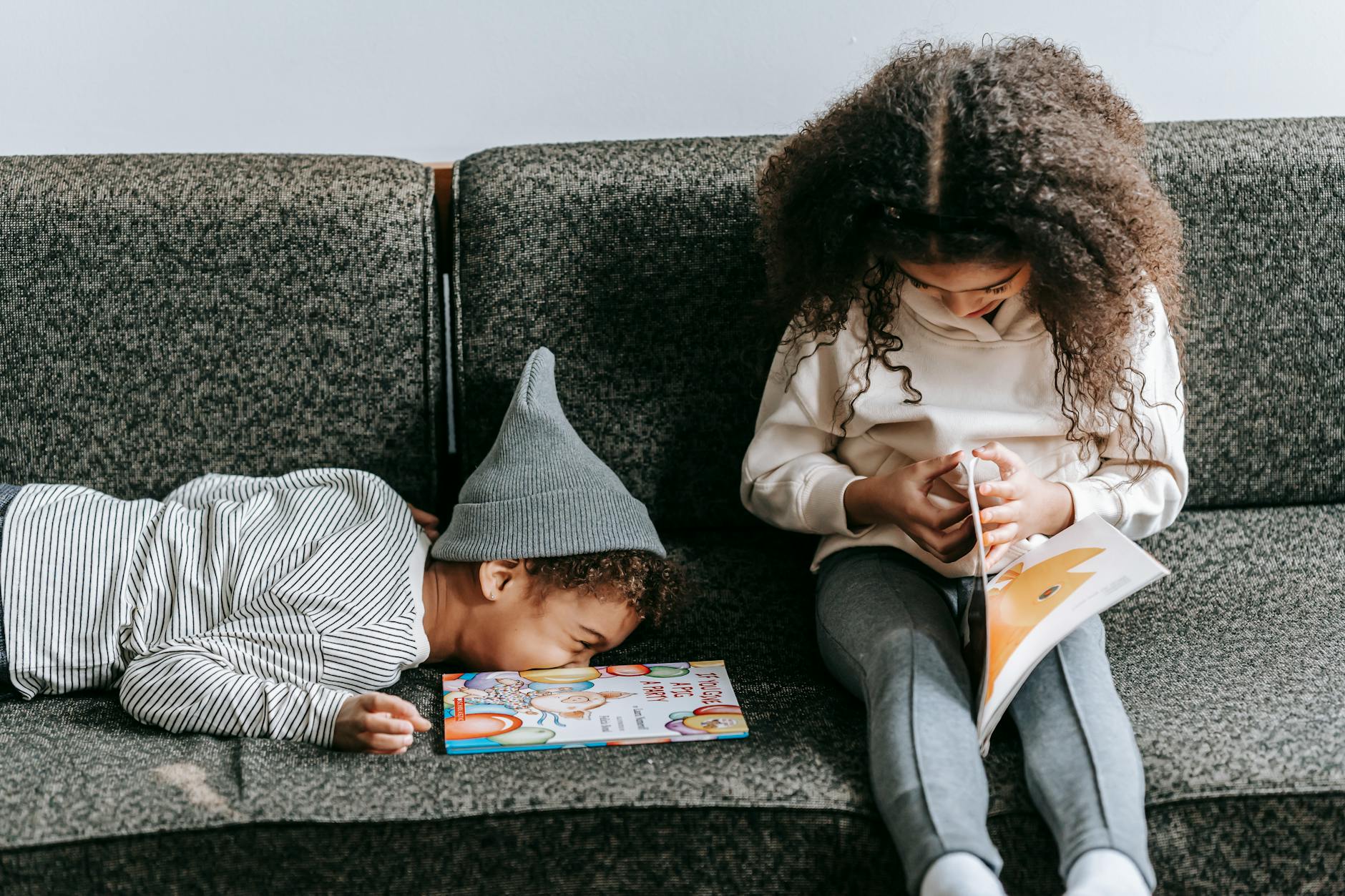 Joyful stylish African American boy lying on cozy couch near cute sister reading interesting book - sibling rivalry quotes