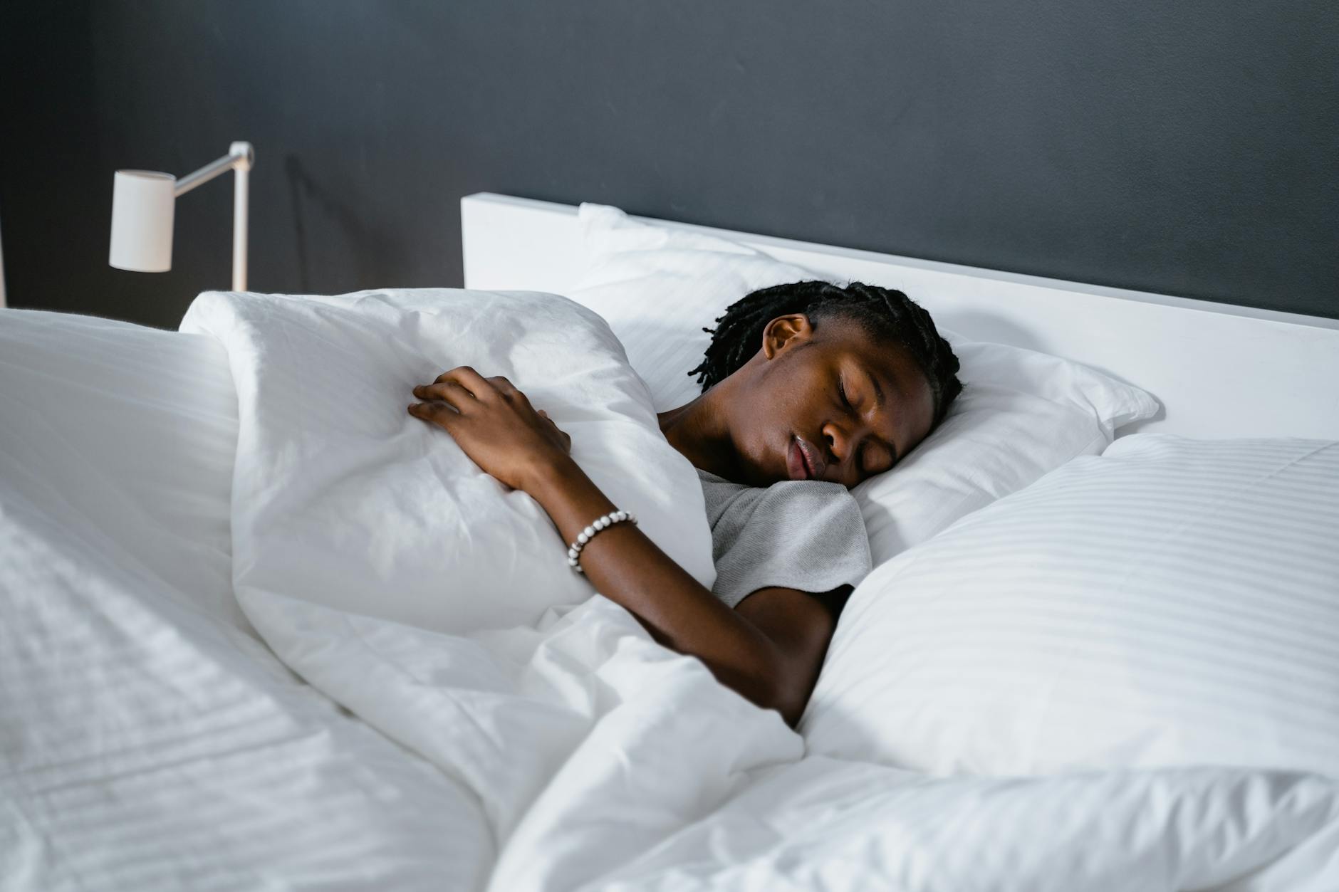 A man sleeping peacefully under a white blanket in a cozy bedroom. - sleep hygiene tips
