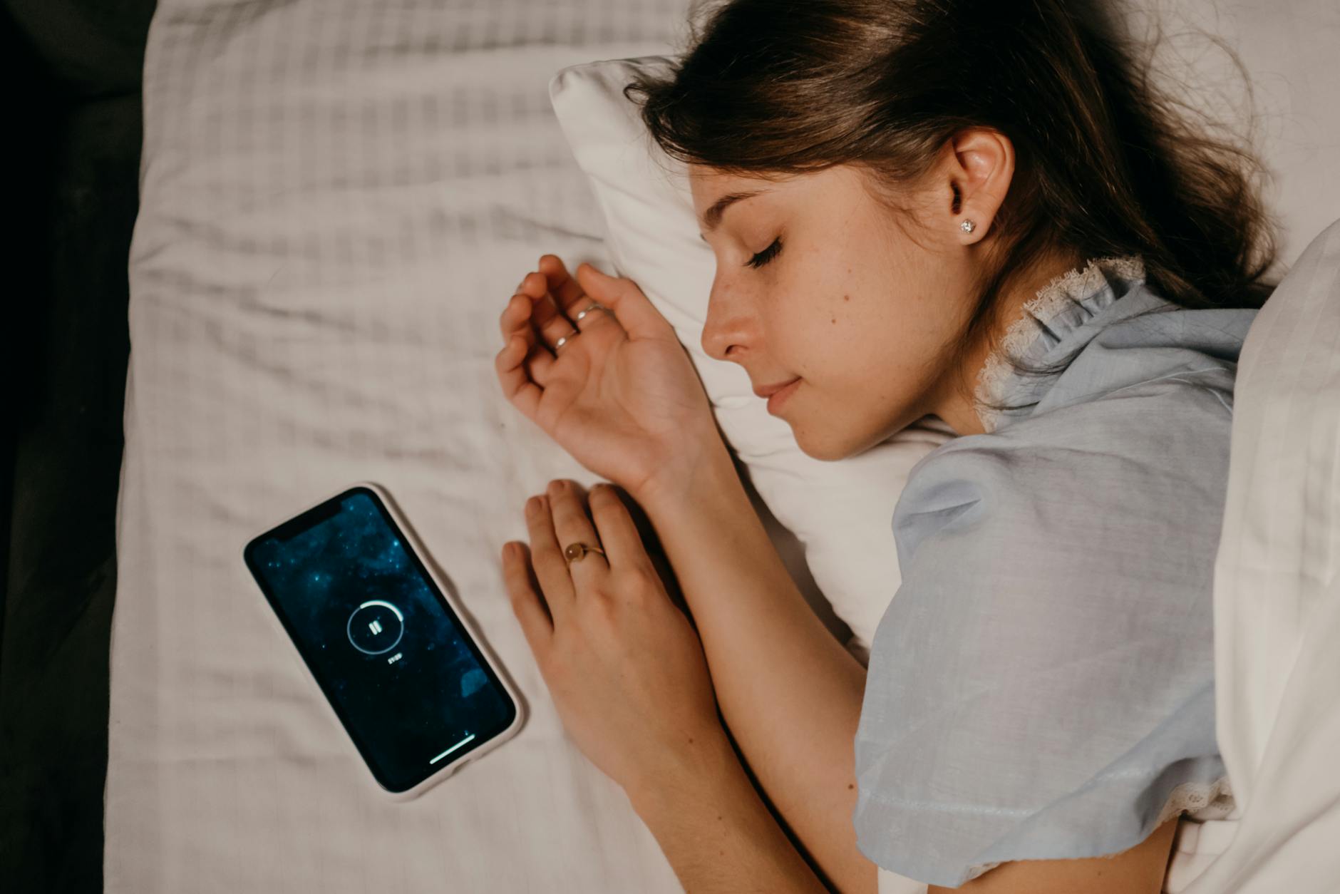 A woman peacefully sleeps in bed with a smartphone beside her, illustrating modern bedtime habits. - sleep hygiene tips