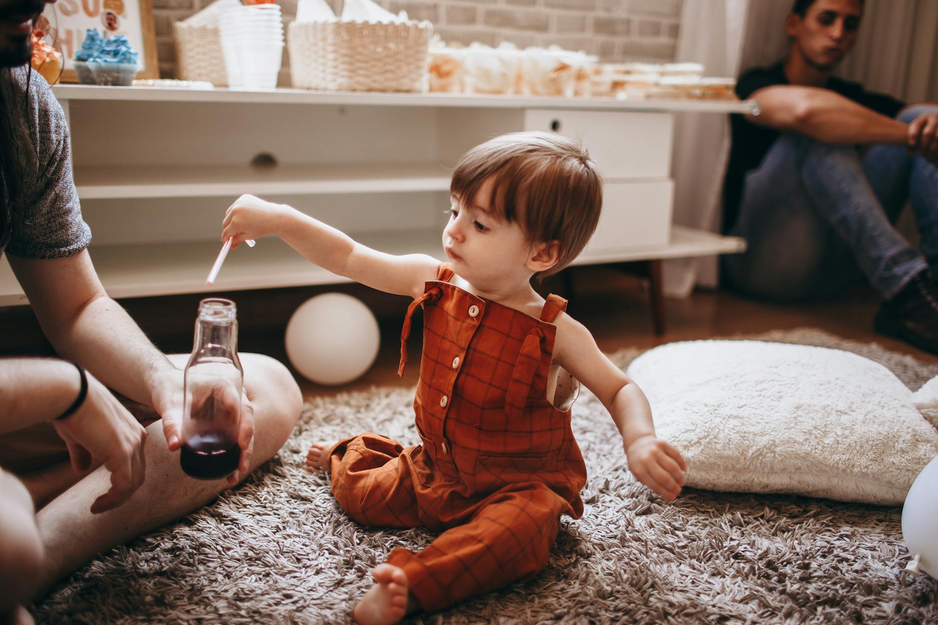 A toddler in an orange romper plays with a bottle indoors. Cozy family setting. - social skills playdates