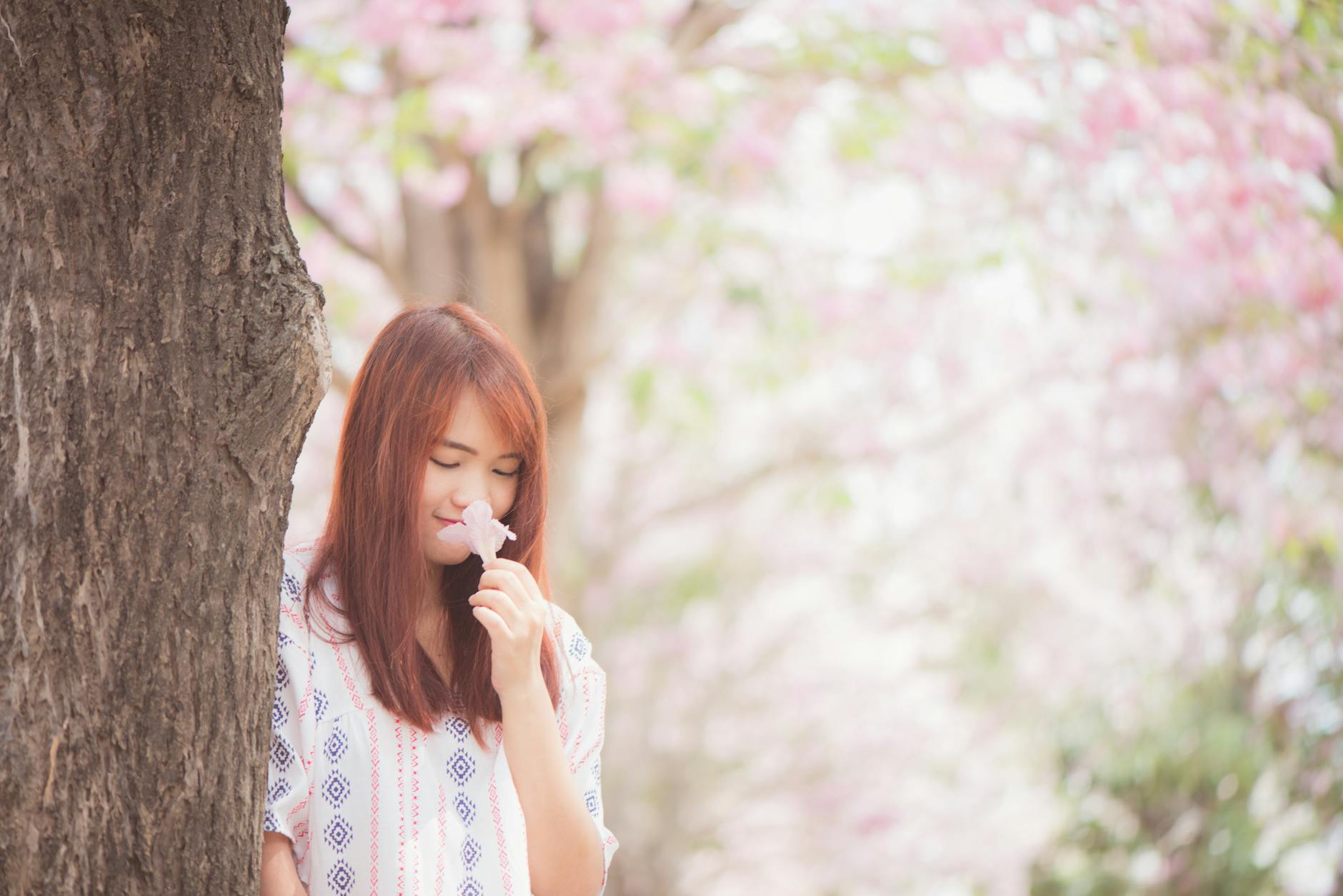A young woman enjoys the scent of cherry blossoms in a serene park setting. - spring allergies anxiety