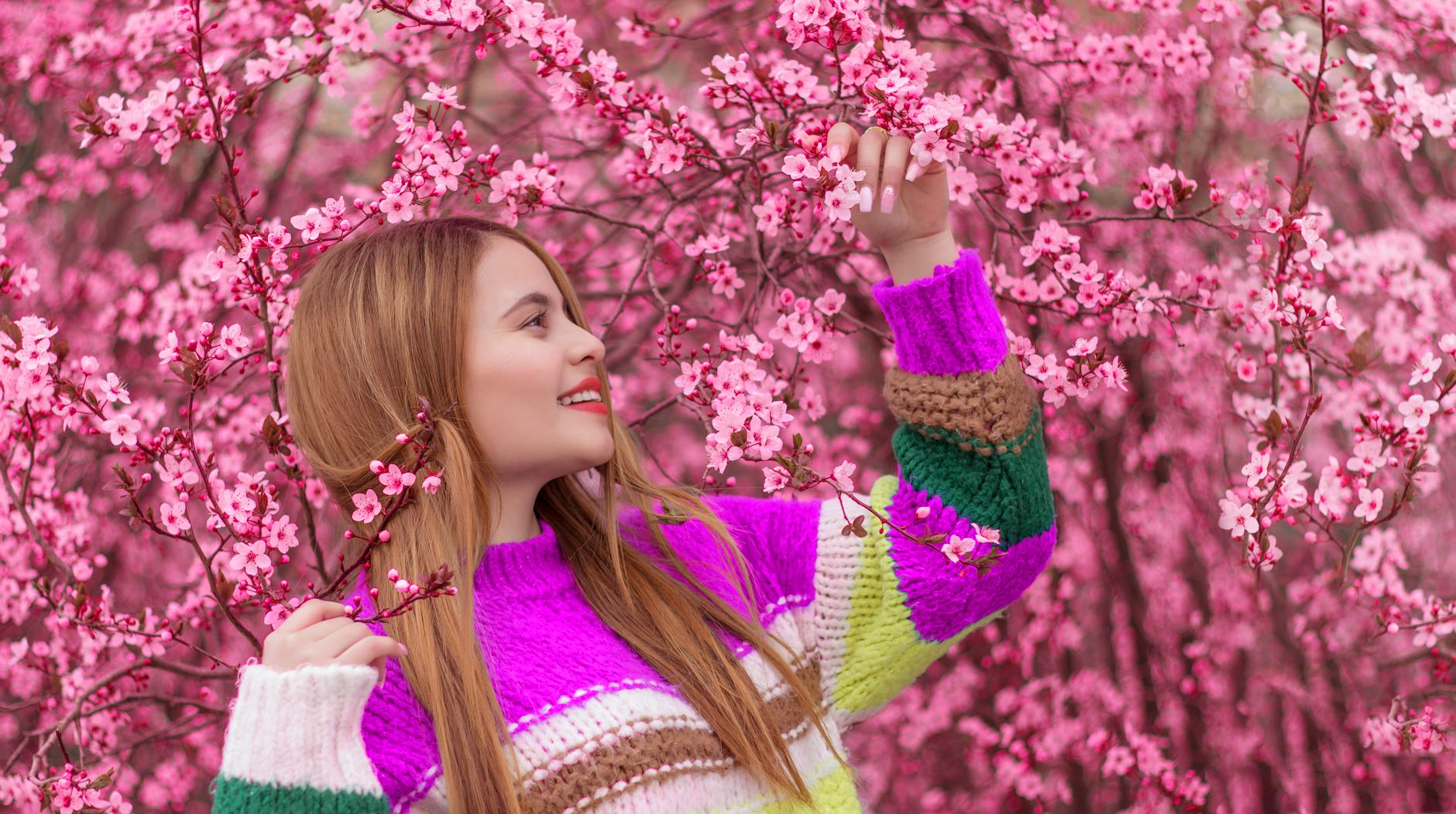 A woman in a colorful sweater enjoying pink cherry blossoms outdoors, capturing spring's beauty. - spring allergy anxiety