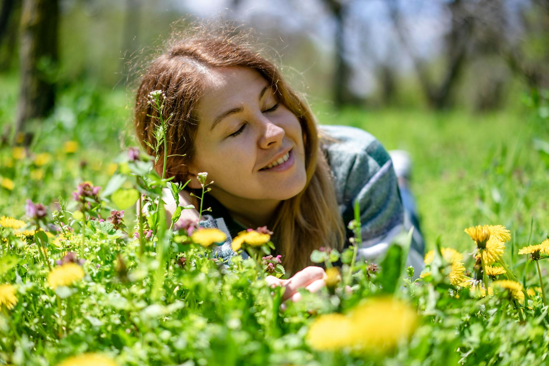 Woman enjoying a sunny day lying among blooming spring flowers in a green meadow. - spring anxiety therapy
