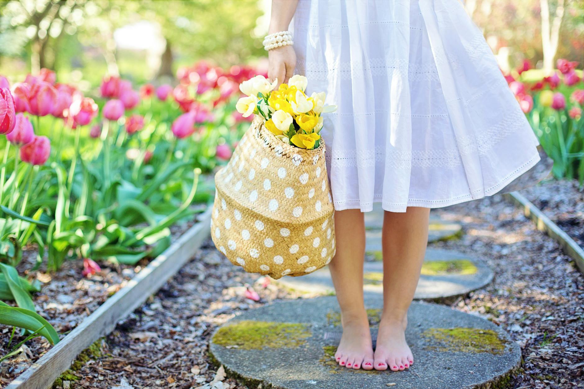A woman in a white dress carries a basket of yellow flowers while walking barefoot in a tulip garden. - spring anxiety therapy