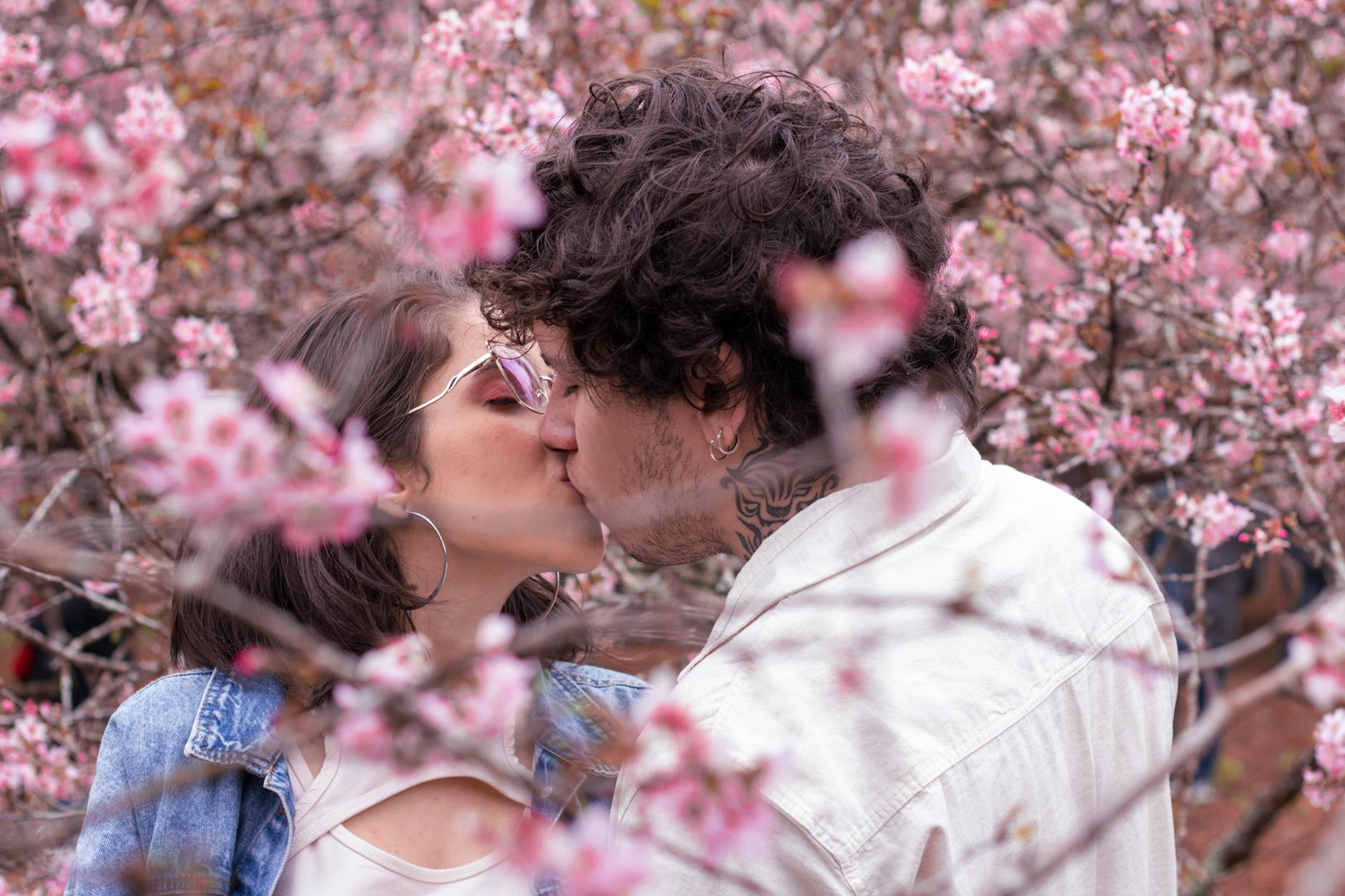 A young couple sharing a kiss surrounded by blooming cherry blossoms in spring. - spring dating ideas