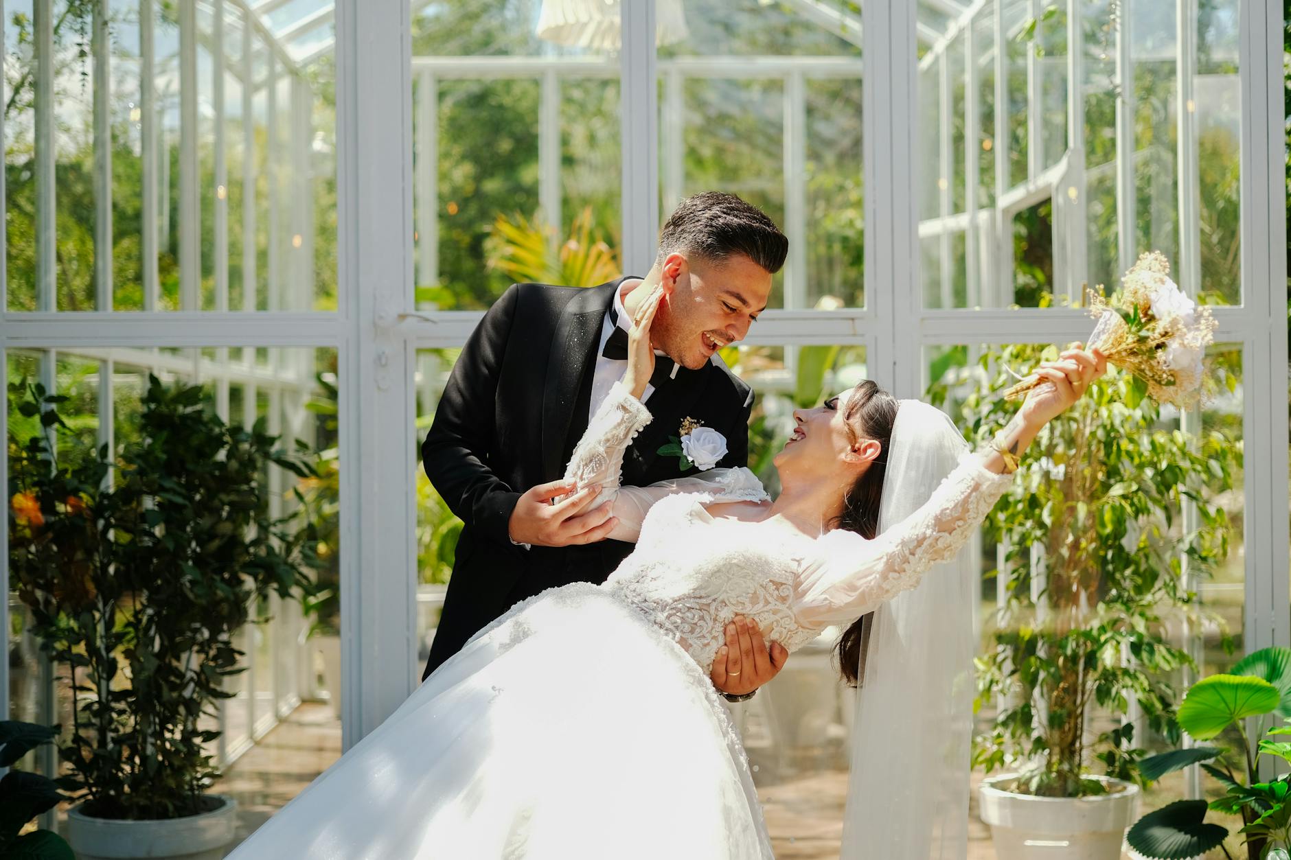 Bride and groom enjoy a romantic moment surrounded by greenery in a bright greenhouse. - spring marriage joy