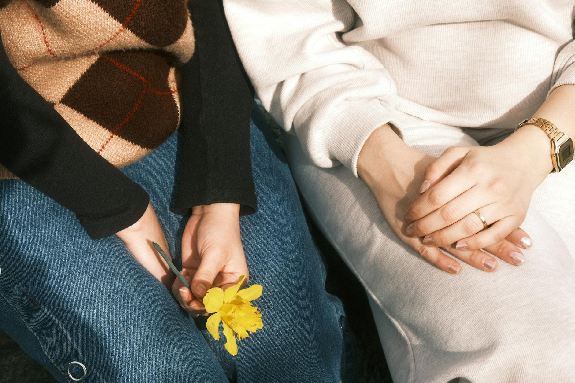Close-up view of two people sitting together, one holding a yellow flower. Ideal for themes of friendship and warmth. - spring sad coping