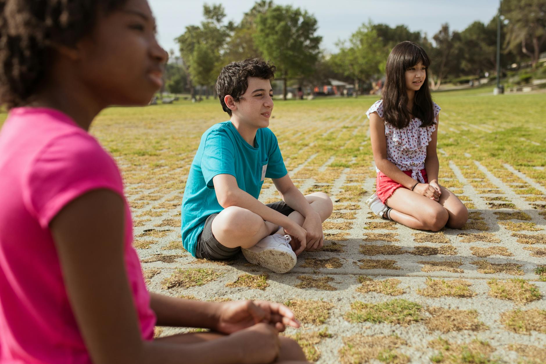 Kids sitting together in a green park during summer camp for team building and fun. - spring social skills