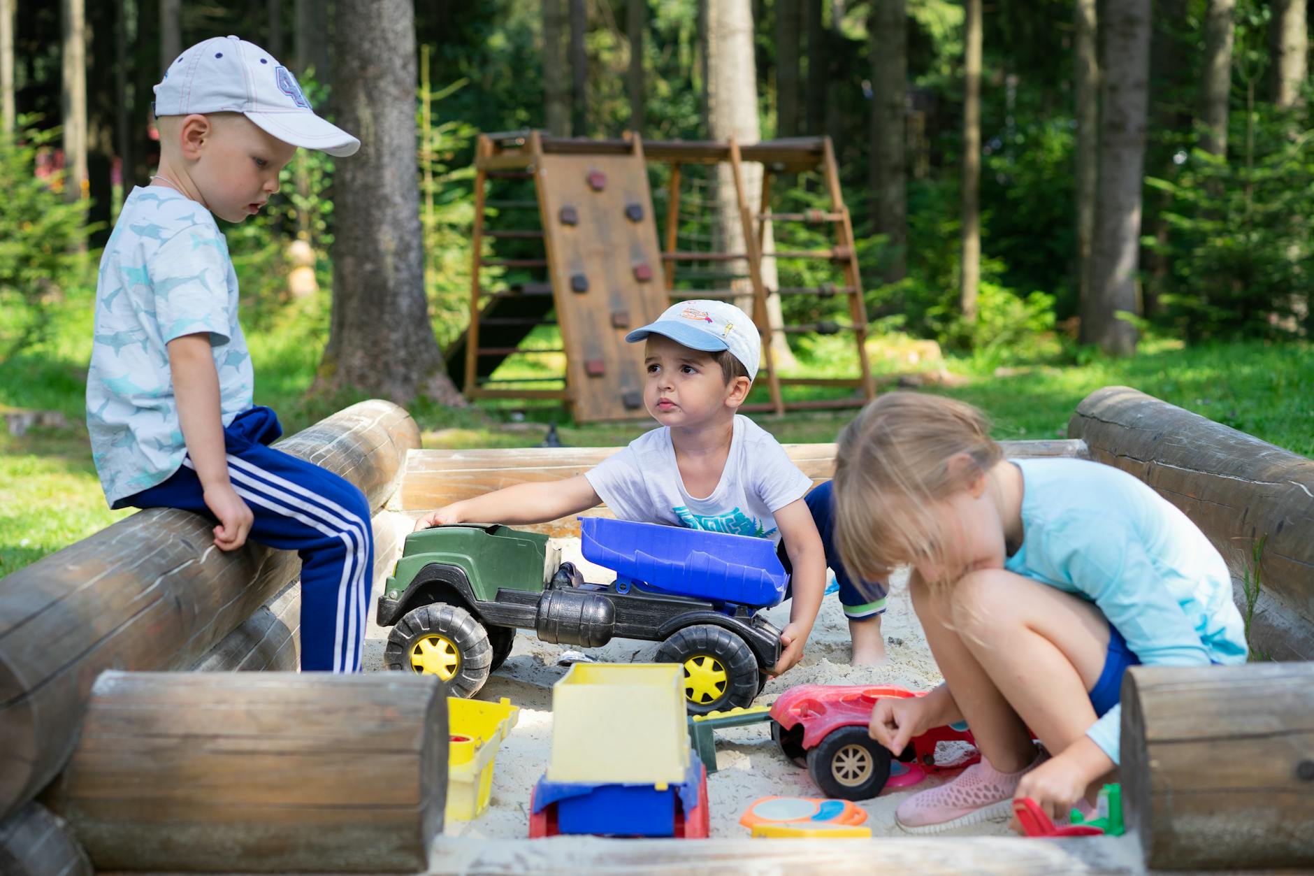 Three children engaged in imaginative play in an outdoor sandbox with toys. - spring social skills