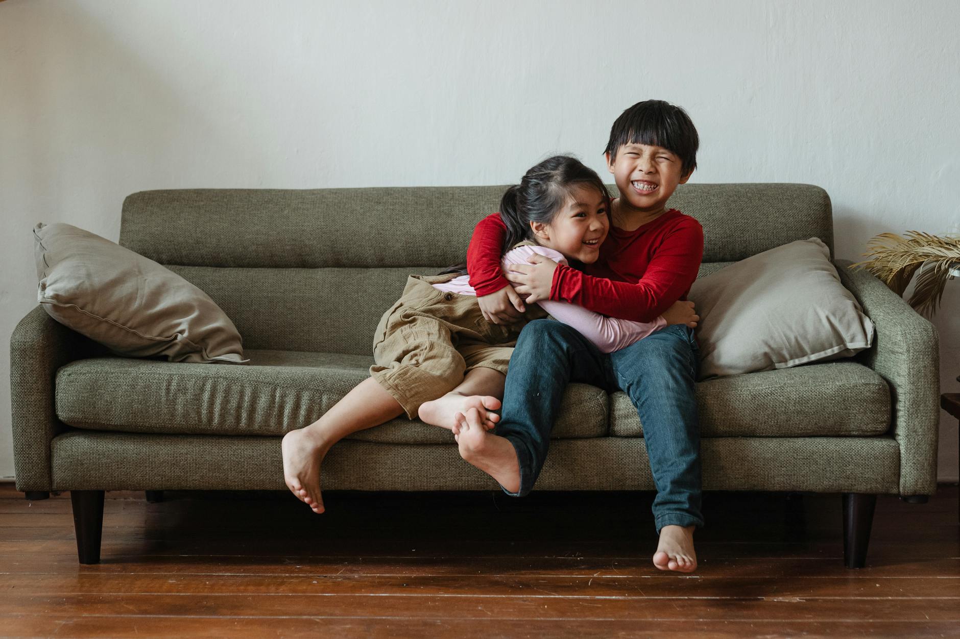 Two happy kids hugging and laughing while sitting on a couch in a cozy living room setting. - step sibling rivalry