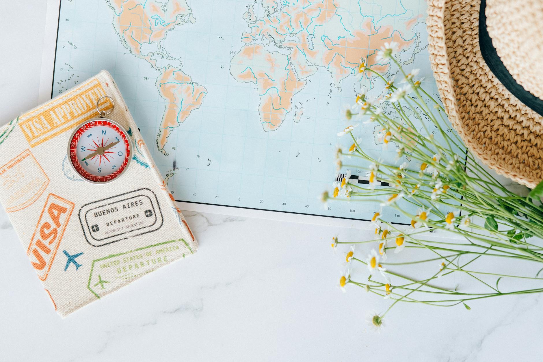 Flat lay of world map, compass, passport, and chamomile flowers, perfect for travel enthusiasts. - summer vacation planning