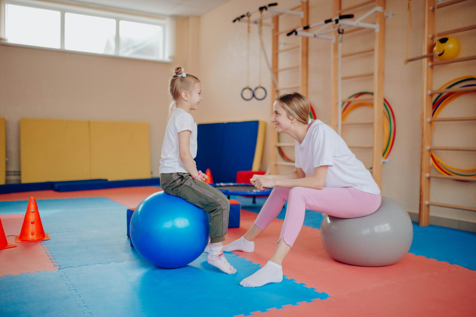 Happy mother and daughter bonding on exercise balls in an indoor gym setting. - therapy integration skills