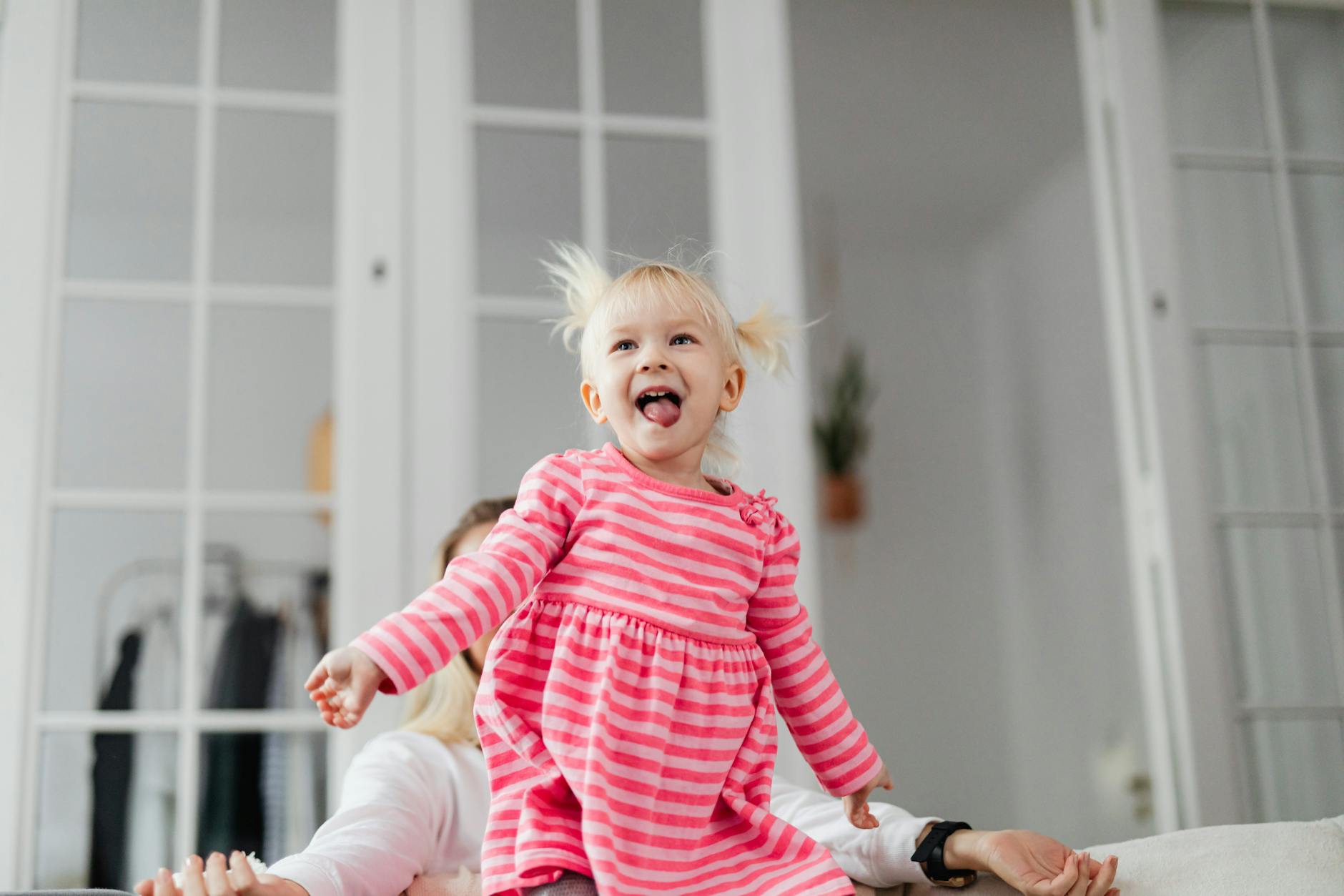 Young girl in pink dress joyfully playing on a couch indoors, full of laughter and fun. - toddler energy bursts