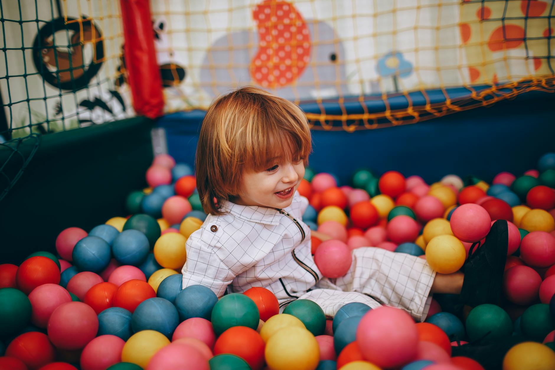 A cheerful child enjoying playtime in a colorful indoor ball pit. - toddler outdoor activities