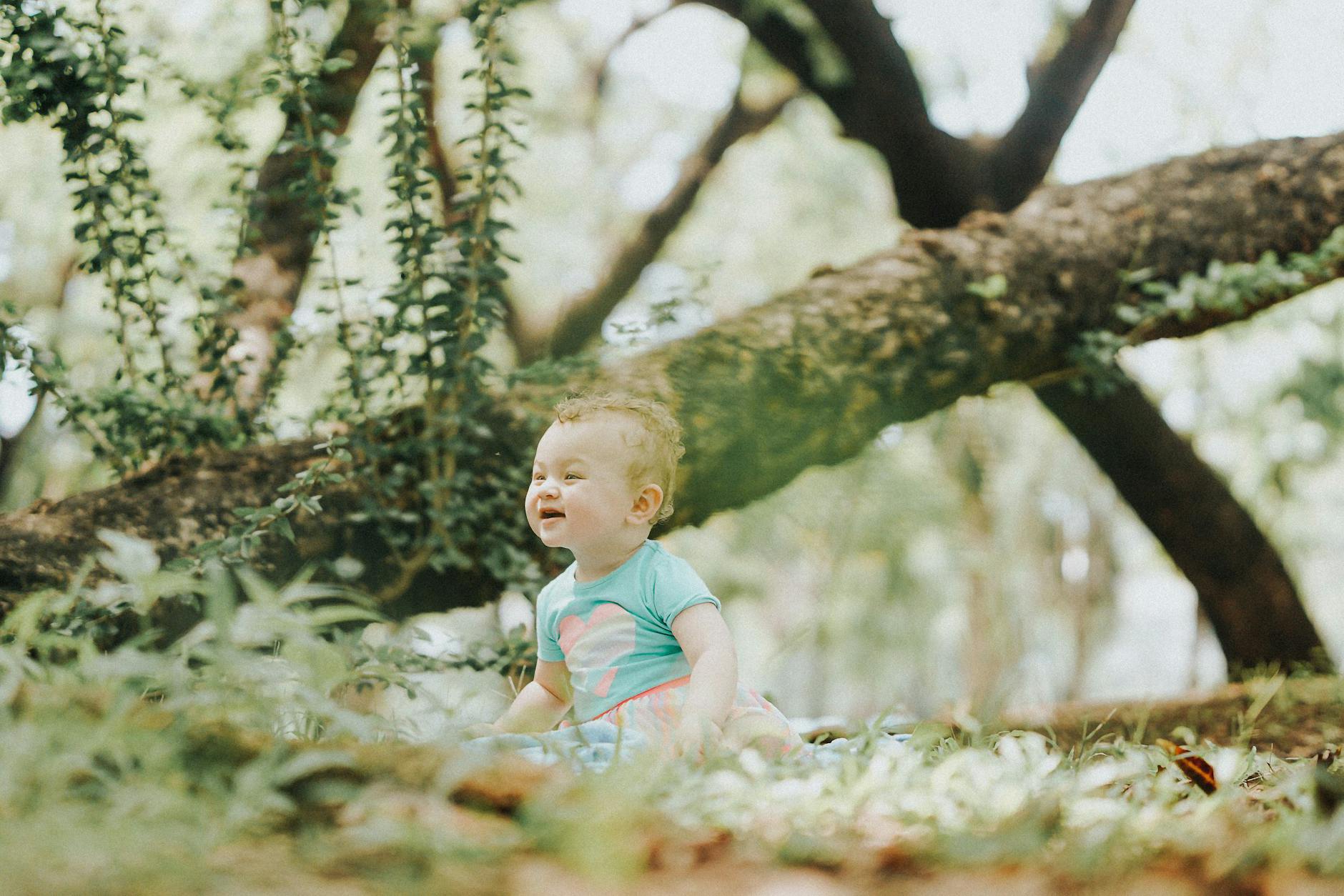 Happy baby enjoying a sunny day sitting on grass in a lush park with a smile. - toddler outdoor exploration