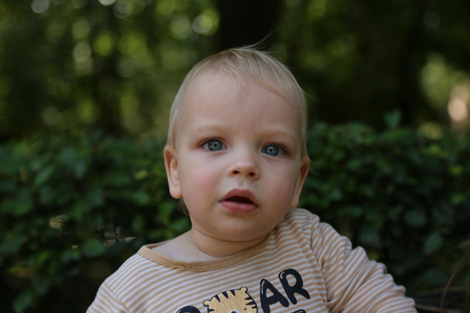 Adorable toddler with blue eyes and blonde hair in a striped shirt, outdoors in Minsk. - toddler spring nature