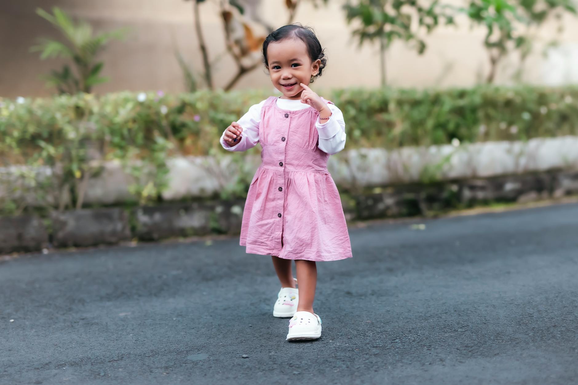 Young child in a pink dress joyfully walking outdoors with a smile. - toddler tantrums outdoors