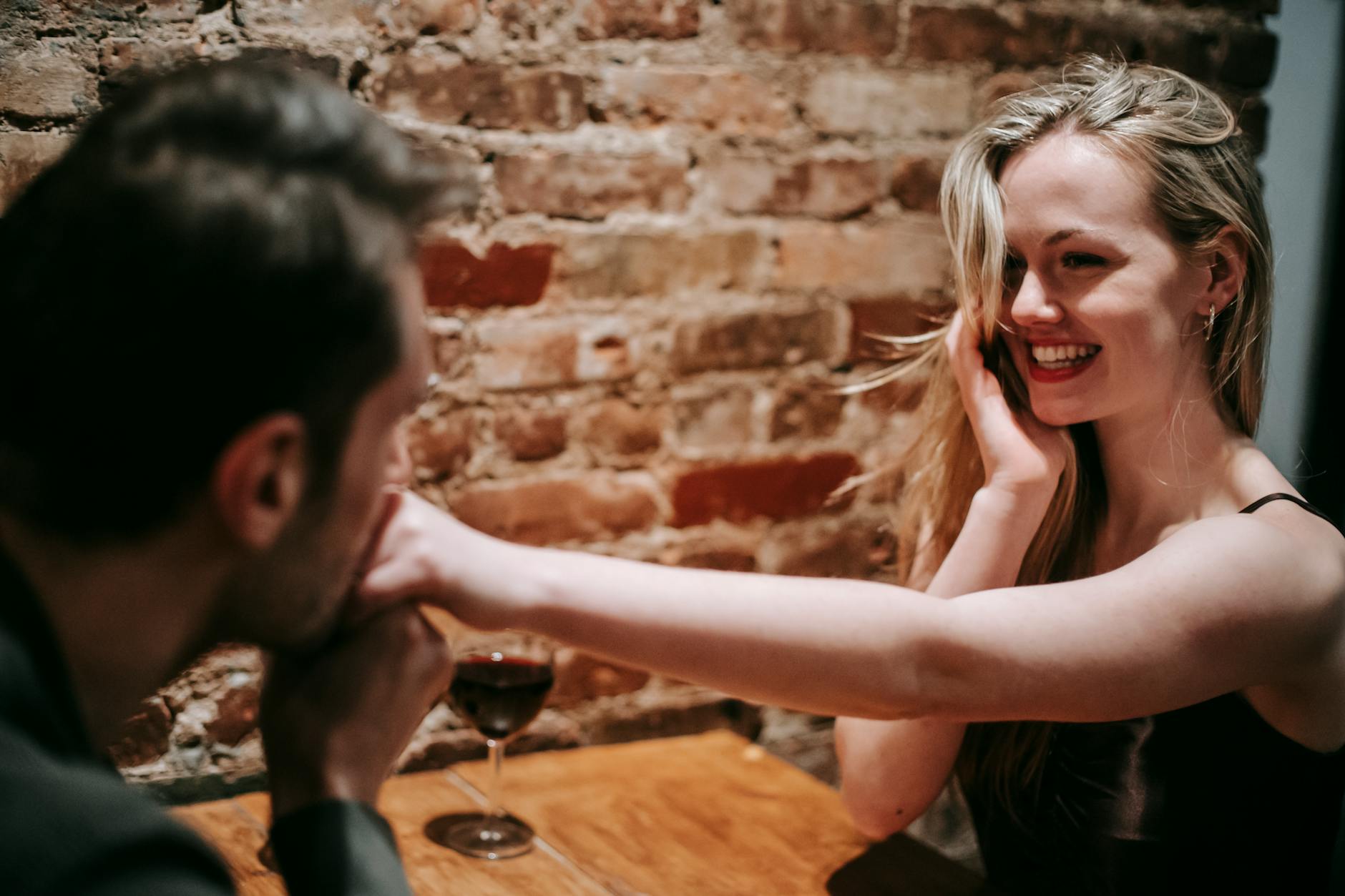 Unrecognizable young man kissing hand of young cheerful blond woman sitting at table in cafe - vulnerable dating