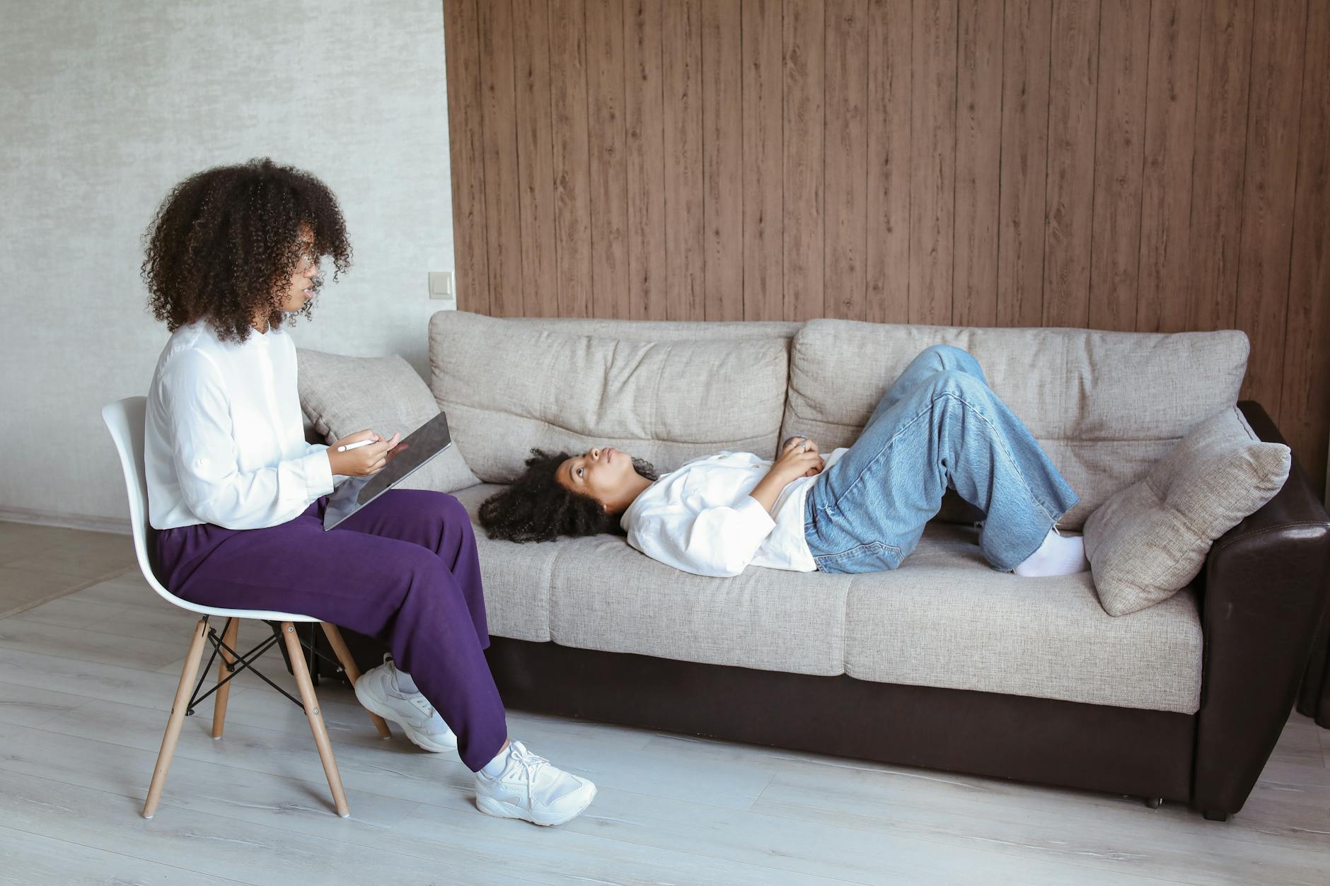 Therapist with a tablet consulting a client lying on a sofa during a counseling session. - attachment style therapist