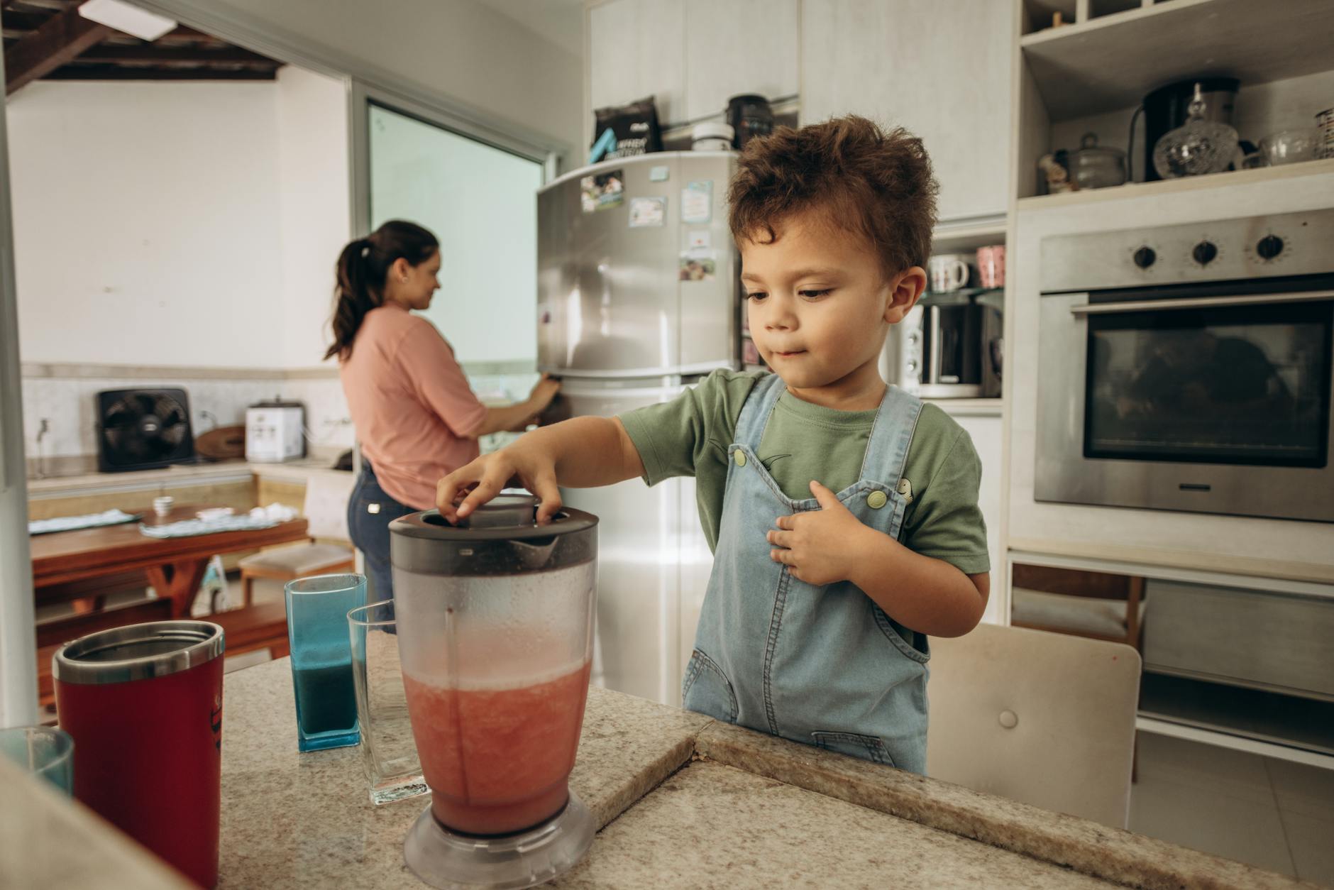 A young boy helps his mother make a smoothie using a blender in a modern kitchen. - blended family summer