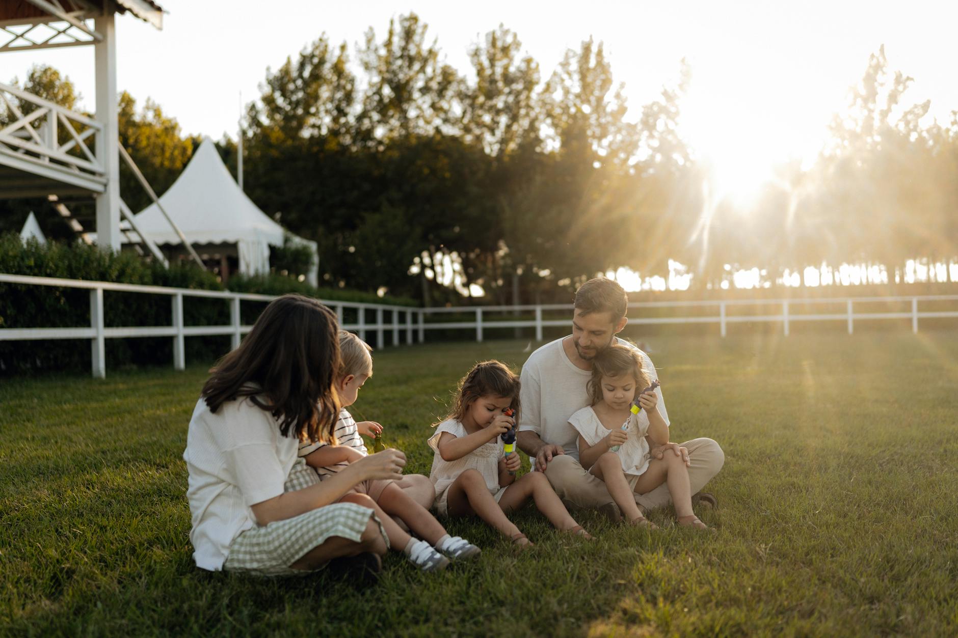 Family sitting on grass enjoying leisure time outdoors, with sun setting in the background. - blended family summer