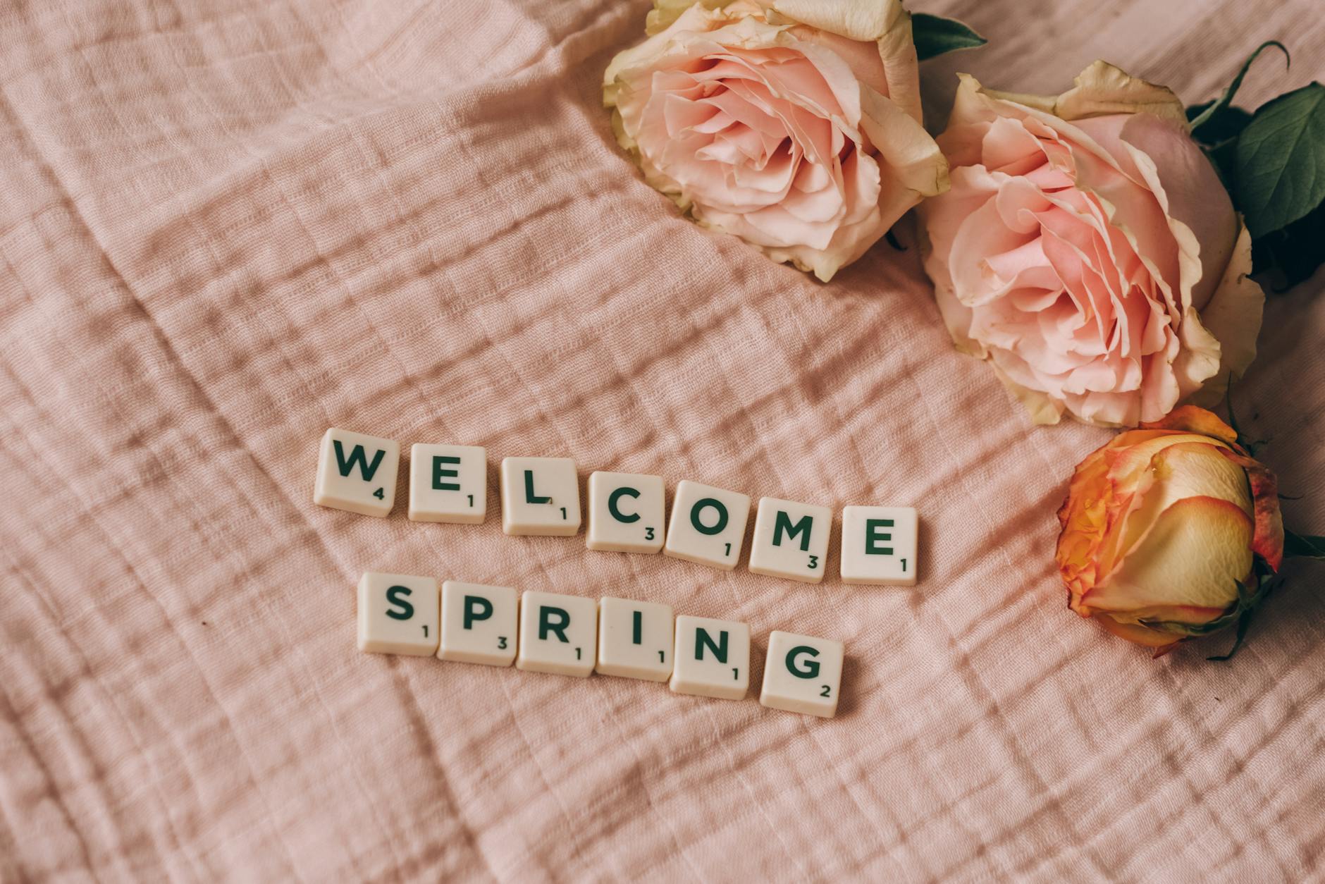 Pink roses and scrabble tiles spelling 'Welcome Spring' on a soft pink fabric background. - cbt for spring anxiety