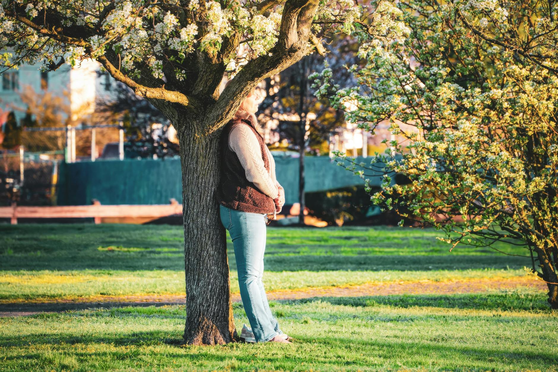 A woman leans against a flowering tree in a sunny park, enjoying a peaceful spring day outdoors. - cbt for spring blues