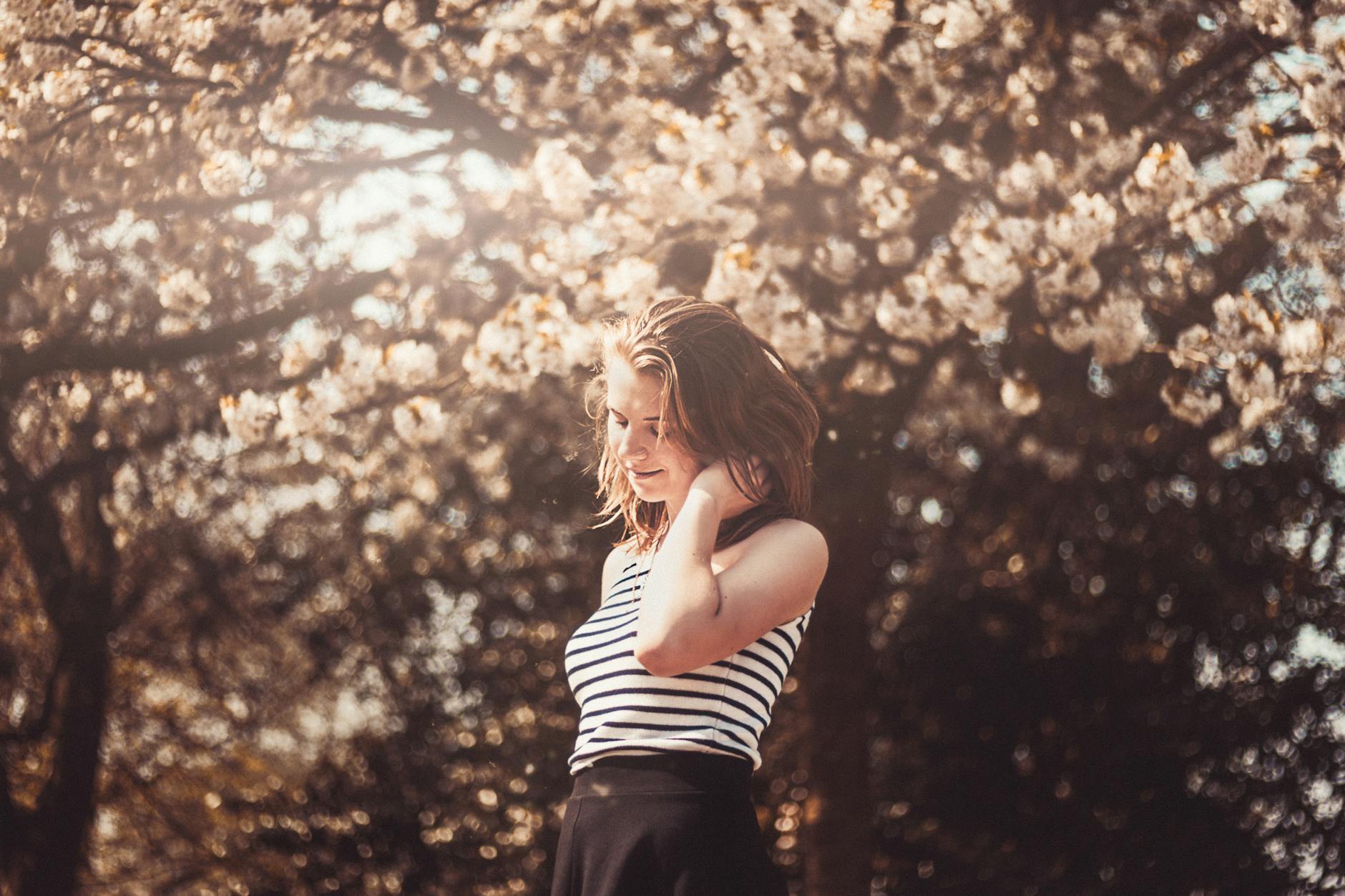 A young woman in a striped shirt enjoying the blooming cherry blossoms outdoors. - cbt for spring blues
