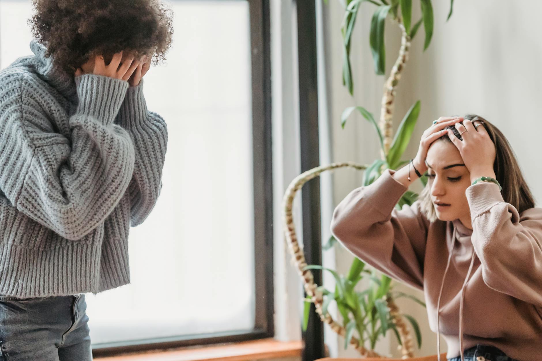 Anonymous female covering face with hands while standing in light room with sad female touching head during conflict at home - cbt for spring sad