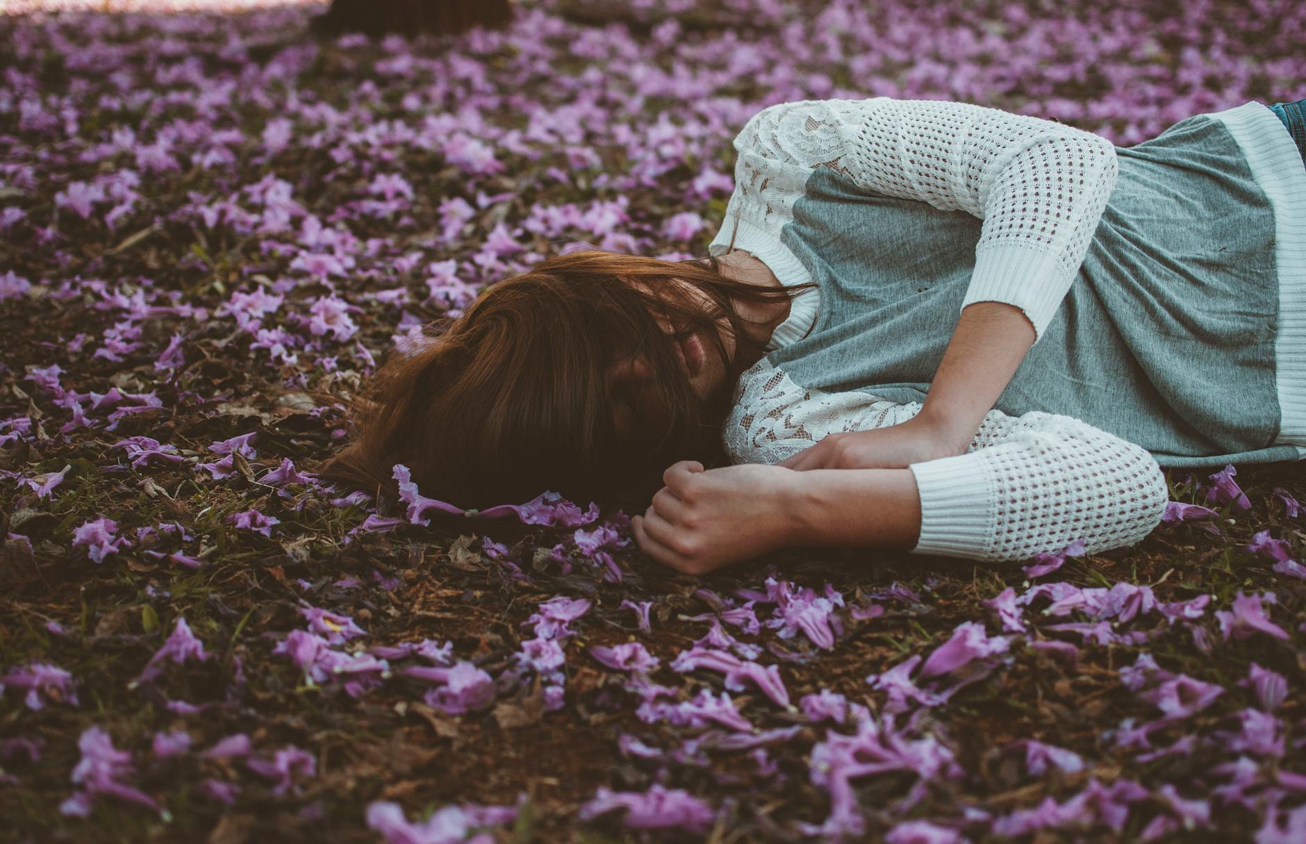 A woman peacefully lies on a field covered with purple flowers, capturing tranquility and nature. - cbt for spring sad