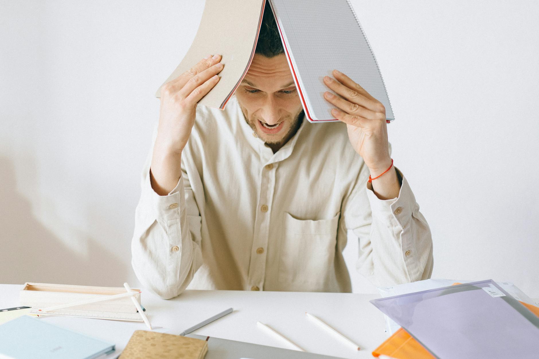 A stressed adult male worker sits at a desk with open notebooks, exhibiting signs of frustration and burnout. - cbt for spring stress