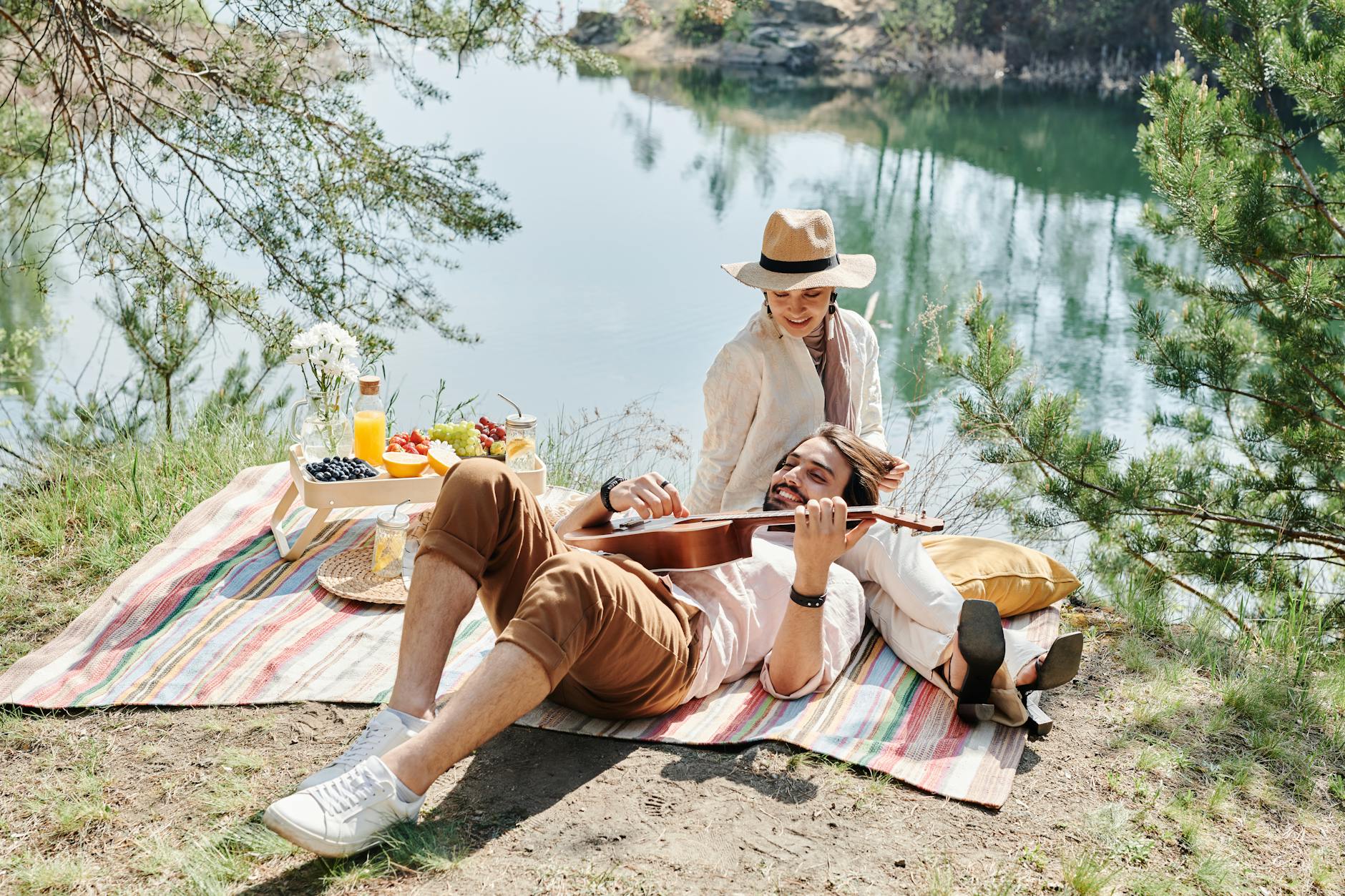 A couple enjoying a serene picnic by the lake, playing ukulele and sharing a joyful moment. - cheap spring dates