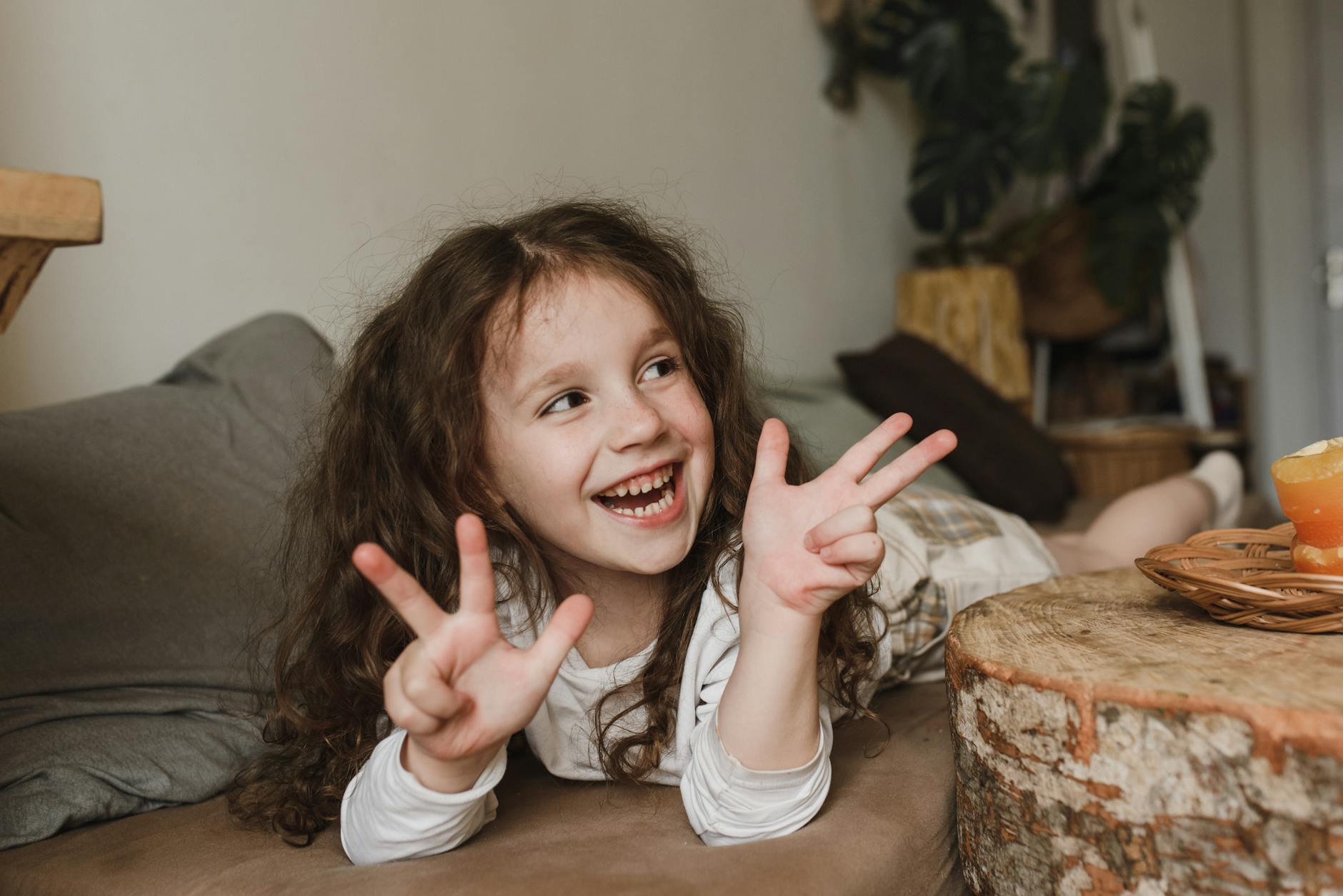 Happy child with curly hair lying on a couch and smiling indoors. - child emotional intelligence