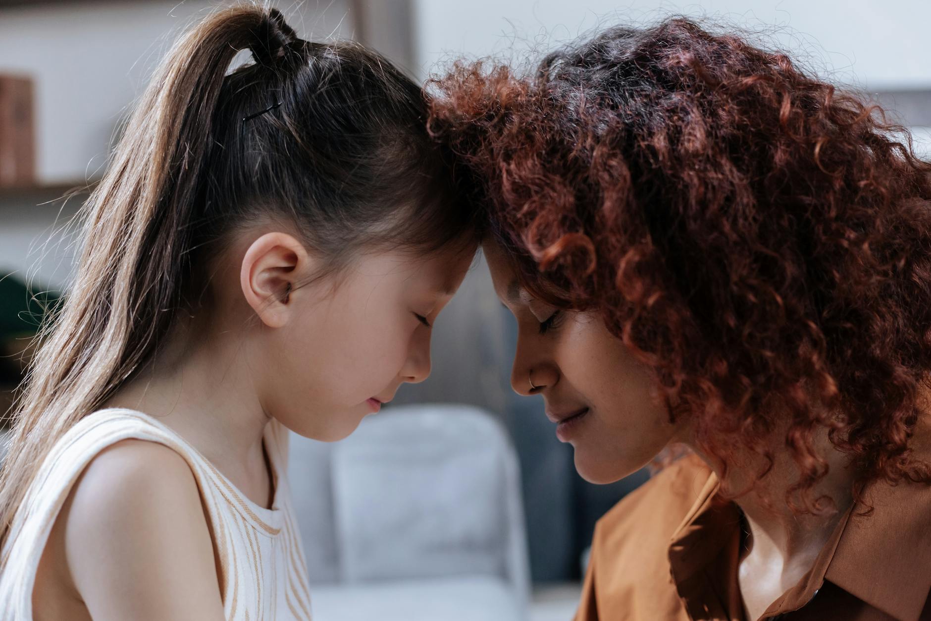 A touching moment between a mother and daughter with foreheads together indoors. - child emotional intelligence