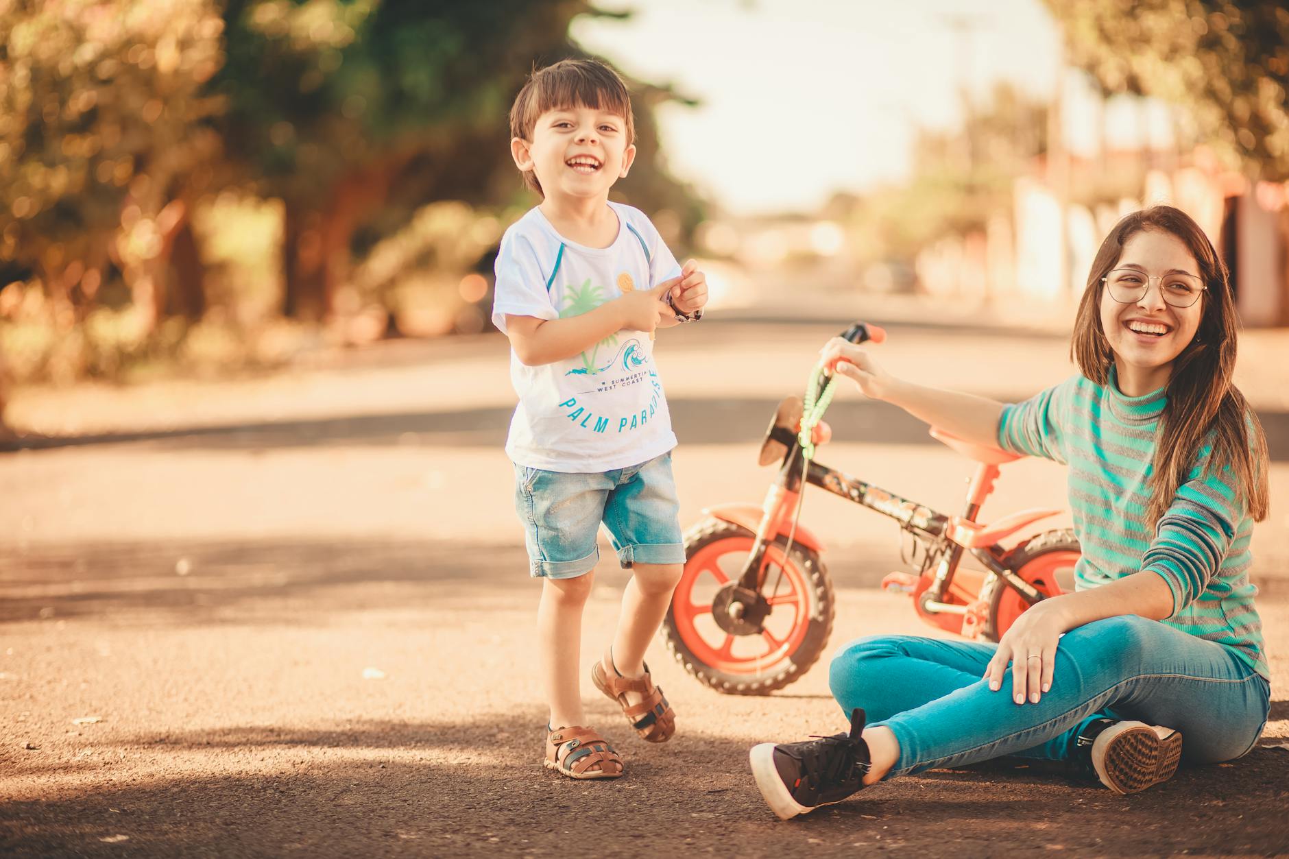 A joyful moment of a mother and son bonding outdoors, enjoying a sunny day with a tricycle. - child resilience summer