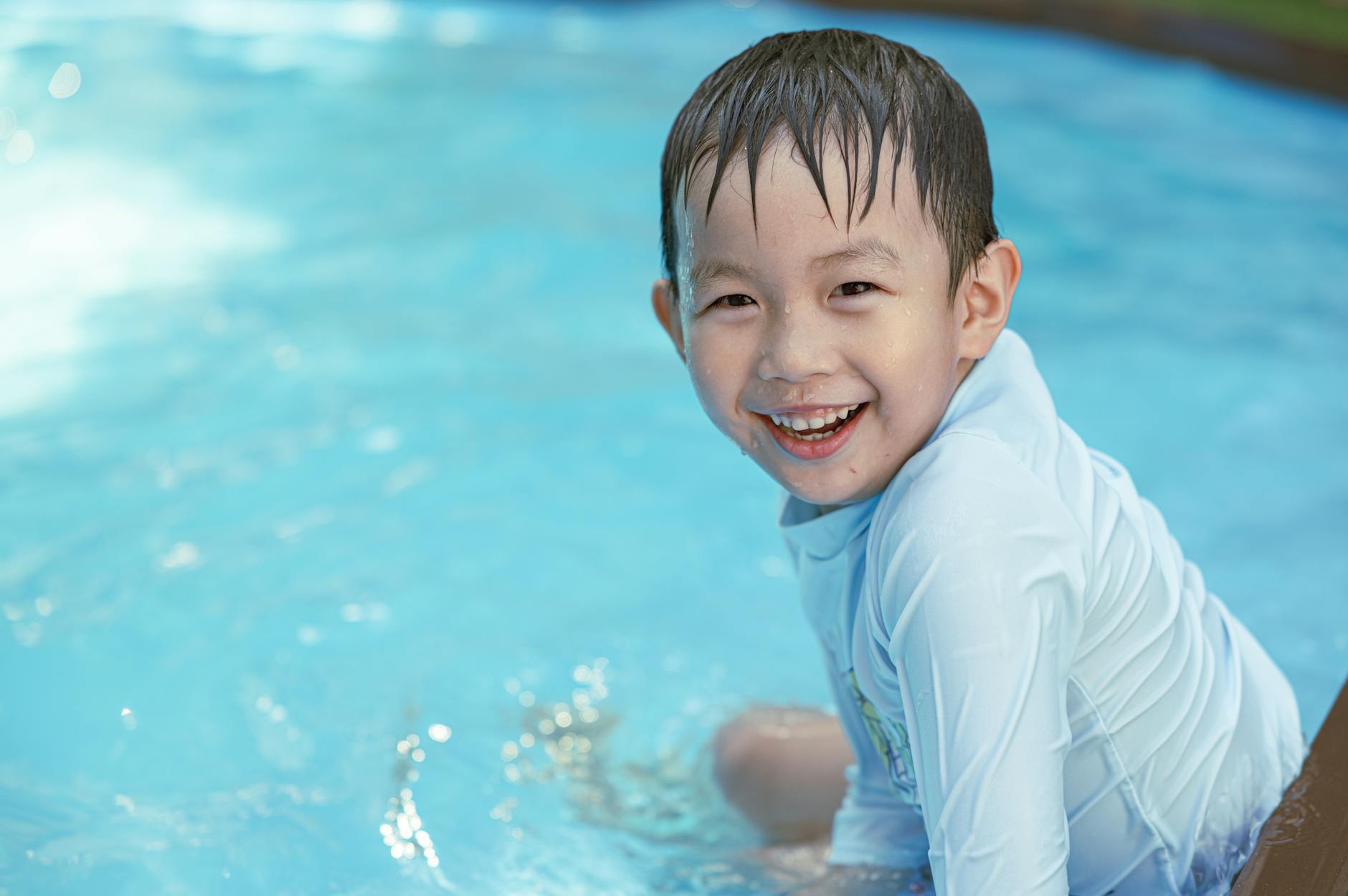 Asian boy smiling brightly while playing in a pool. Perfect summer fun moment. - child resilience summer