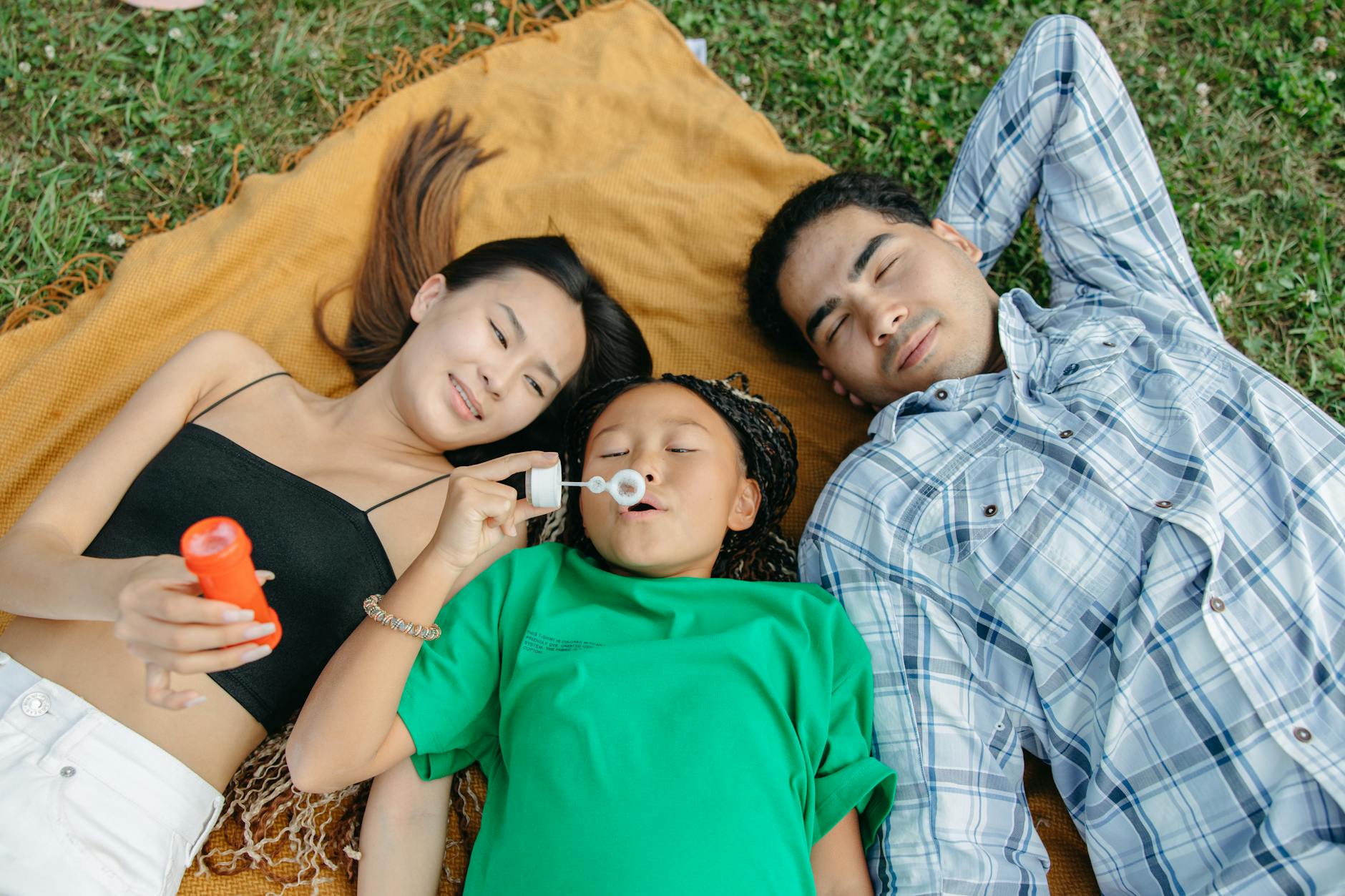 A family lying on a blanket outdoors enjoying a relaxing moment while a child blows bubbles. - co-parenting after break