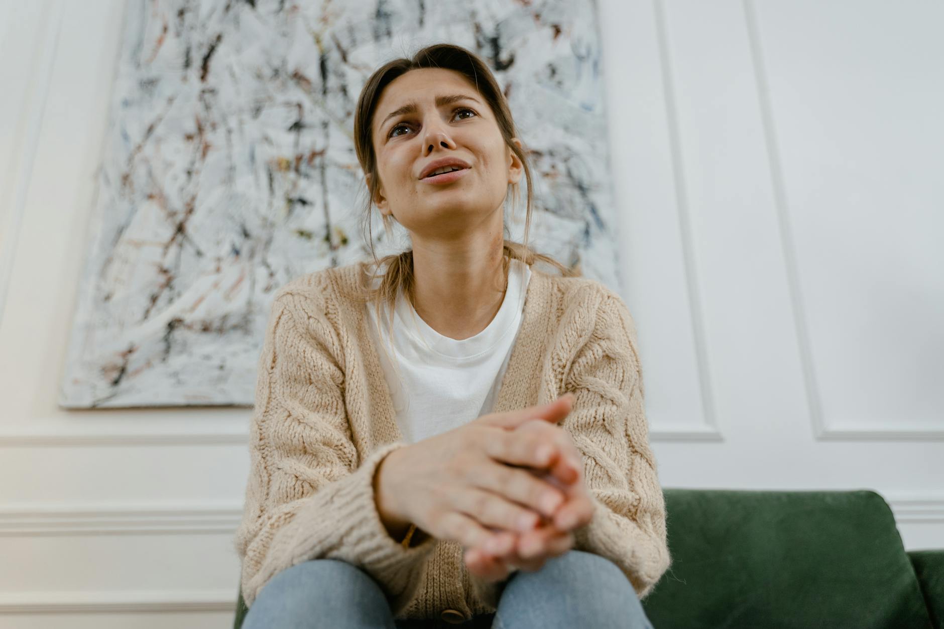 A woman in a cozy sweater is sitting indoors, expressing distress and frustration. - dbt emotional regulation
