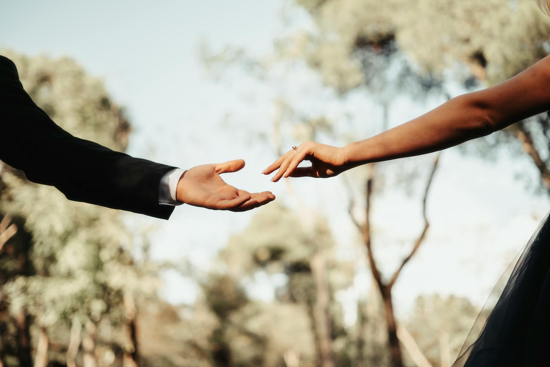 Close-up of a couple's hands reaching towards each other outdoors, evoking romance and connection. - deepen marriage connection