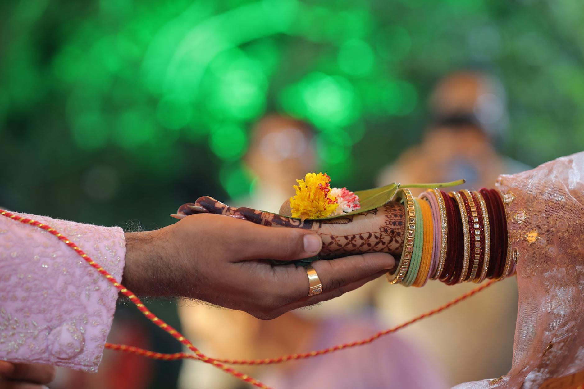 Close-up of hands in a traditional Indian wedding ritual with henna and vibrant bangles. - early marriage connection