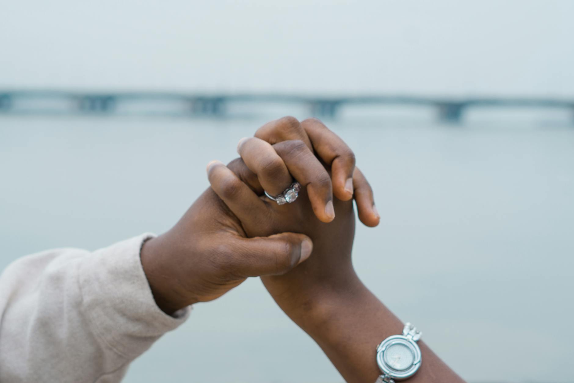 A couple holds hands with engagement ring visible over the bridge in Lagos, Nigeria. - early marriage connection