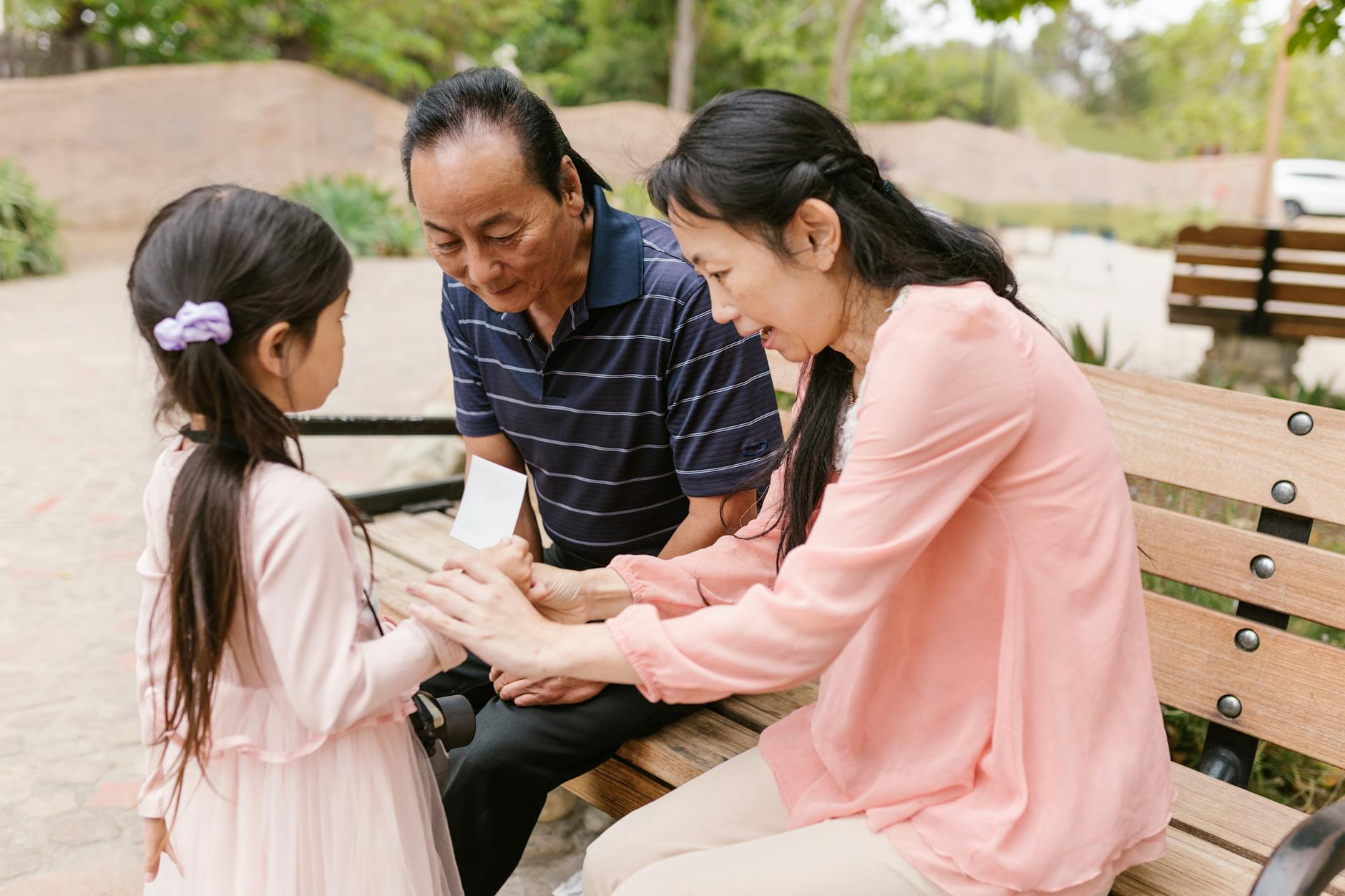 Asian family bonding outdoors, with adults sitting on a bench engaging with a child. - family communication empathy
