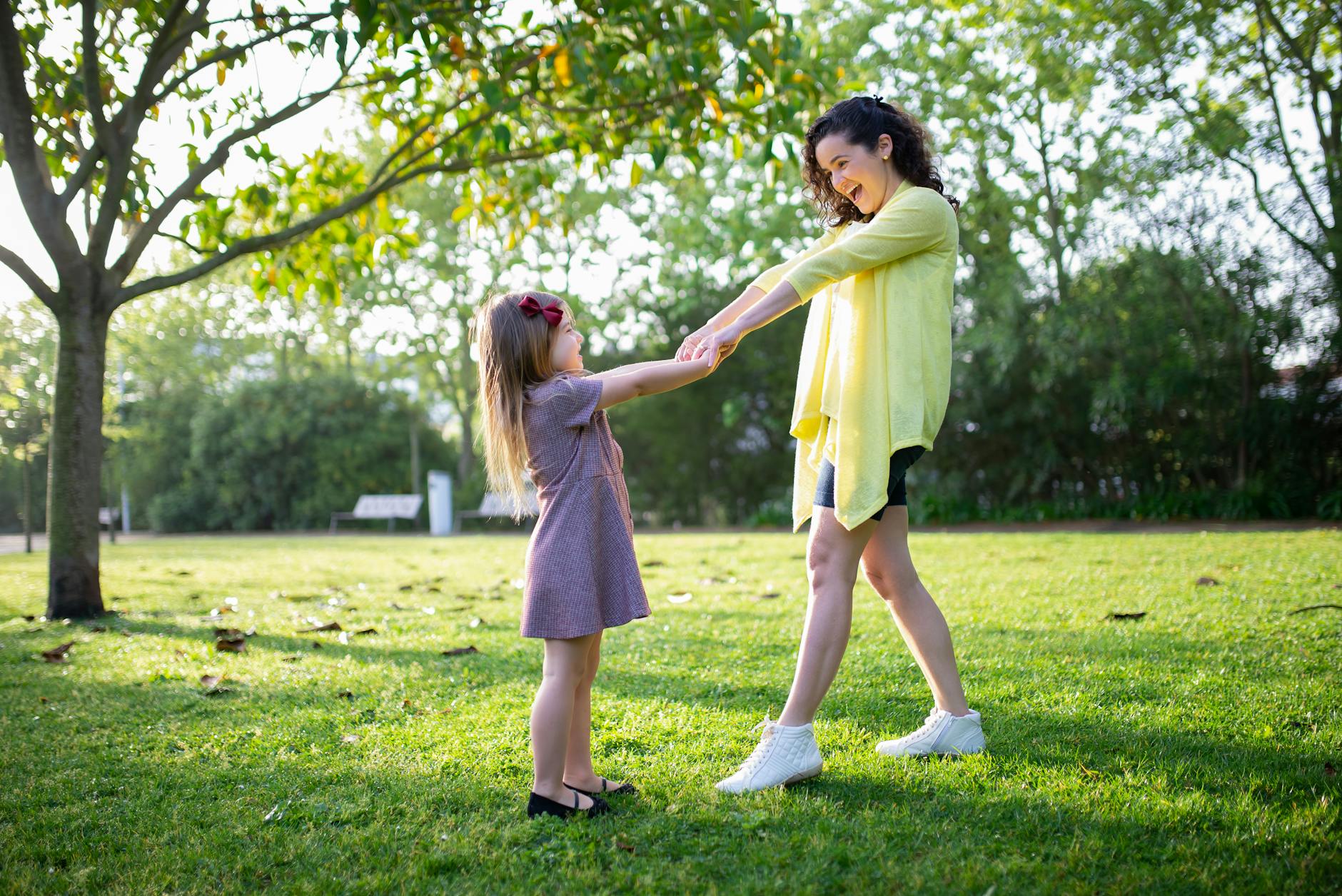 Mother and daughter enjoying a playful moment in a sunny park, holding hands and smiling. - kid resilience spring transition