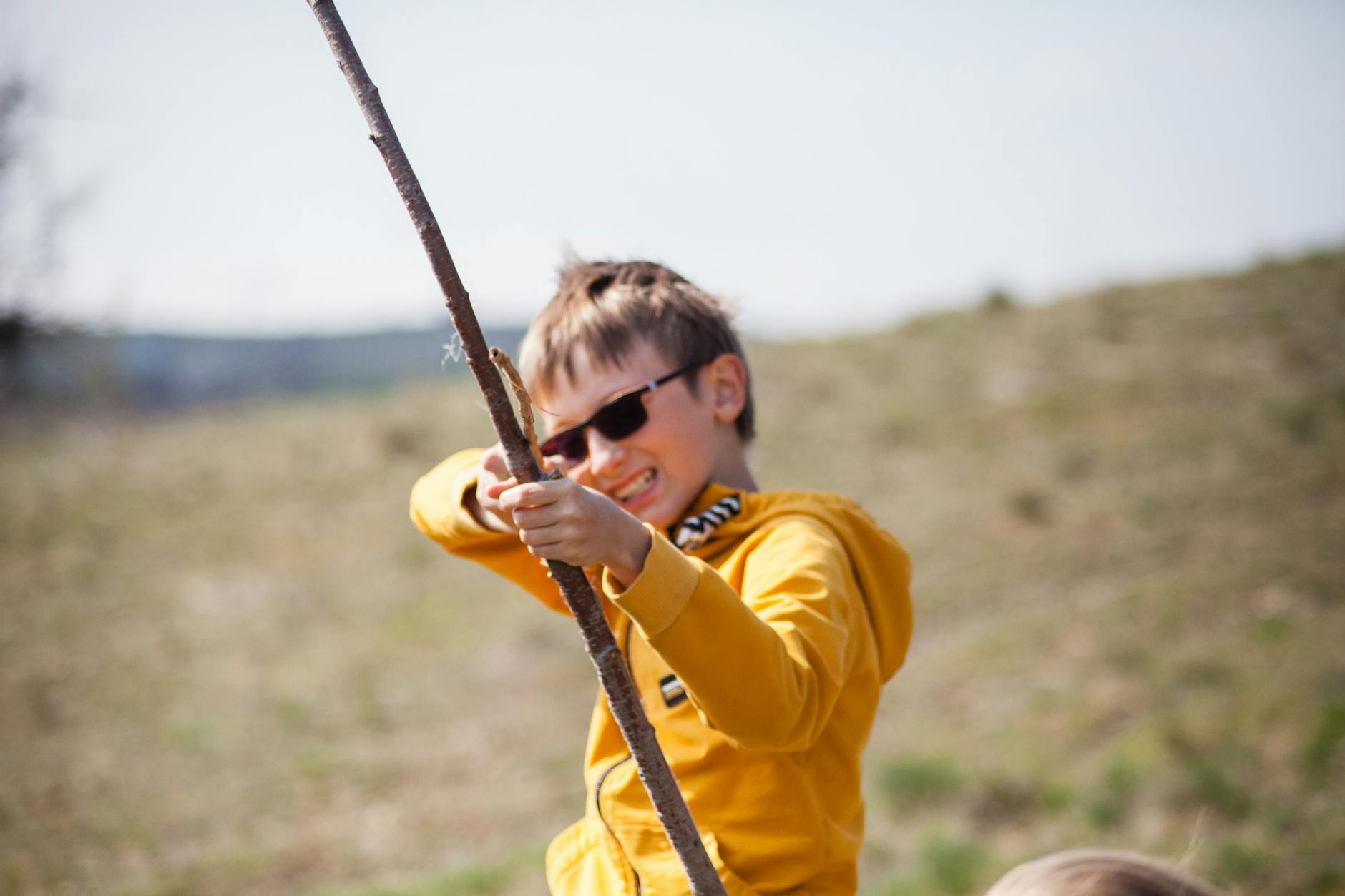 A happy child in sunglasses playing with a stick outdoors, capturing the essence of fun and energy. - kid resilience spring transition