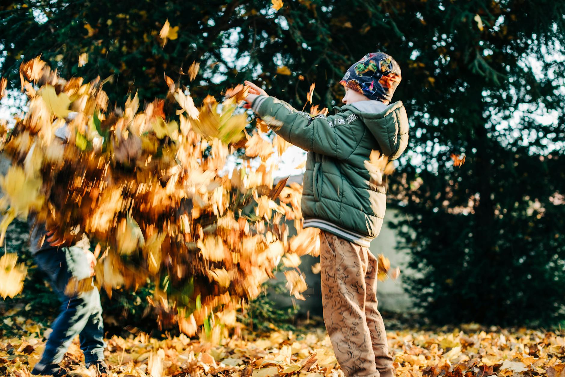 Two children joyfully playing with leaves in a sunlit autumn park setting. - kids cope change