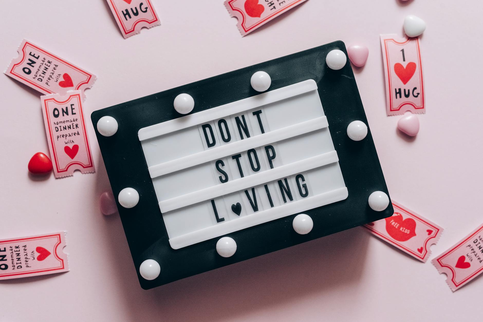 Lightbox with 'Don't Stop Loving' surrounded by hearts and love tokens on pink background. - long distance date ideas